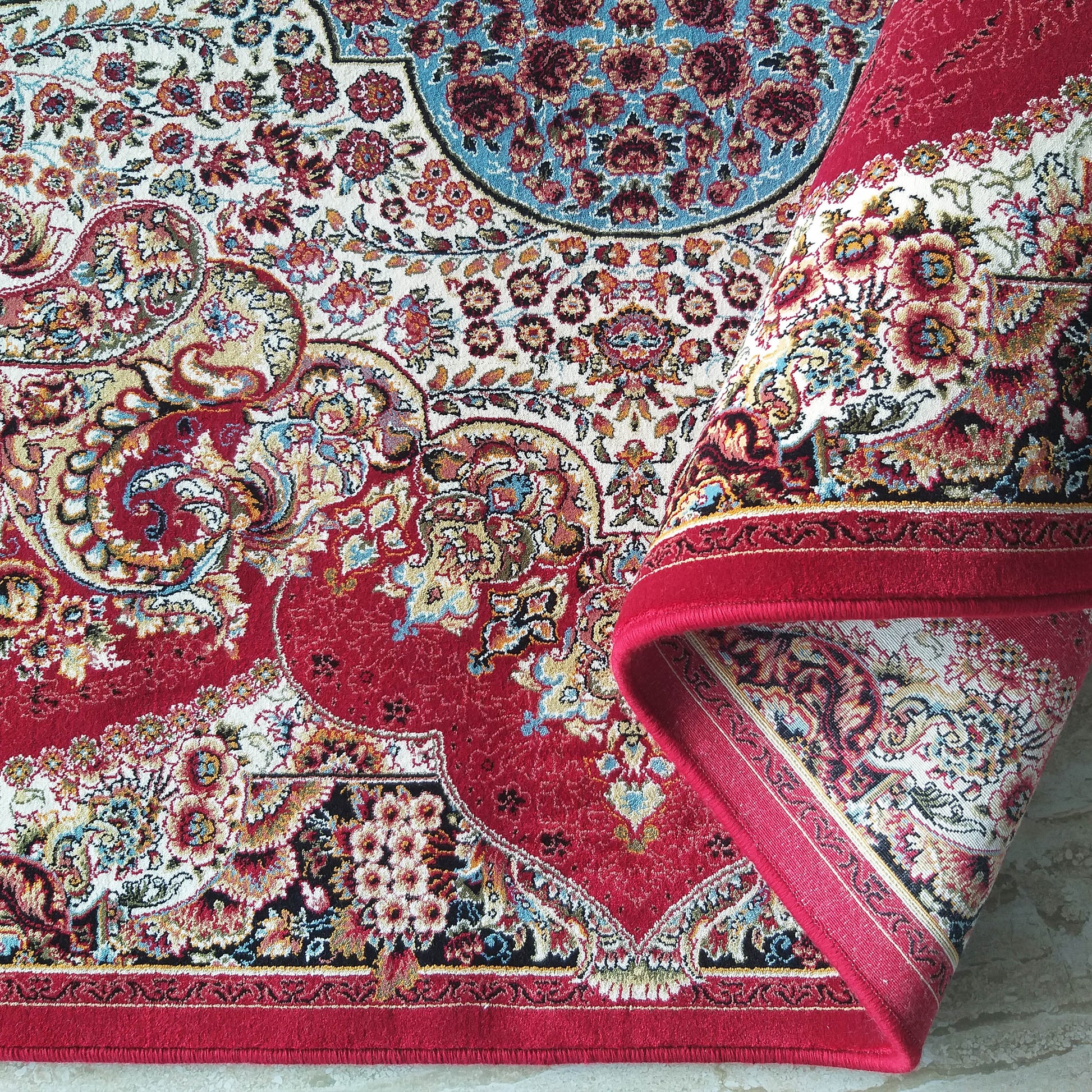 Tapis floral rouge et crème richement orné de motifs cachemire multicolores, une section est enroulée