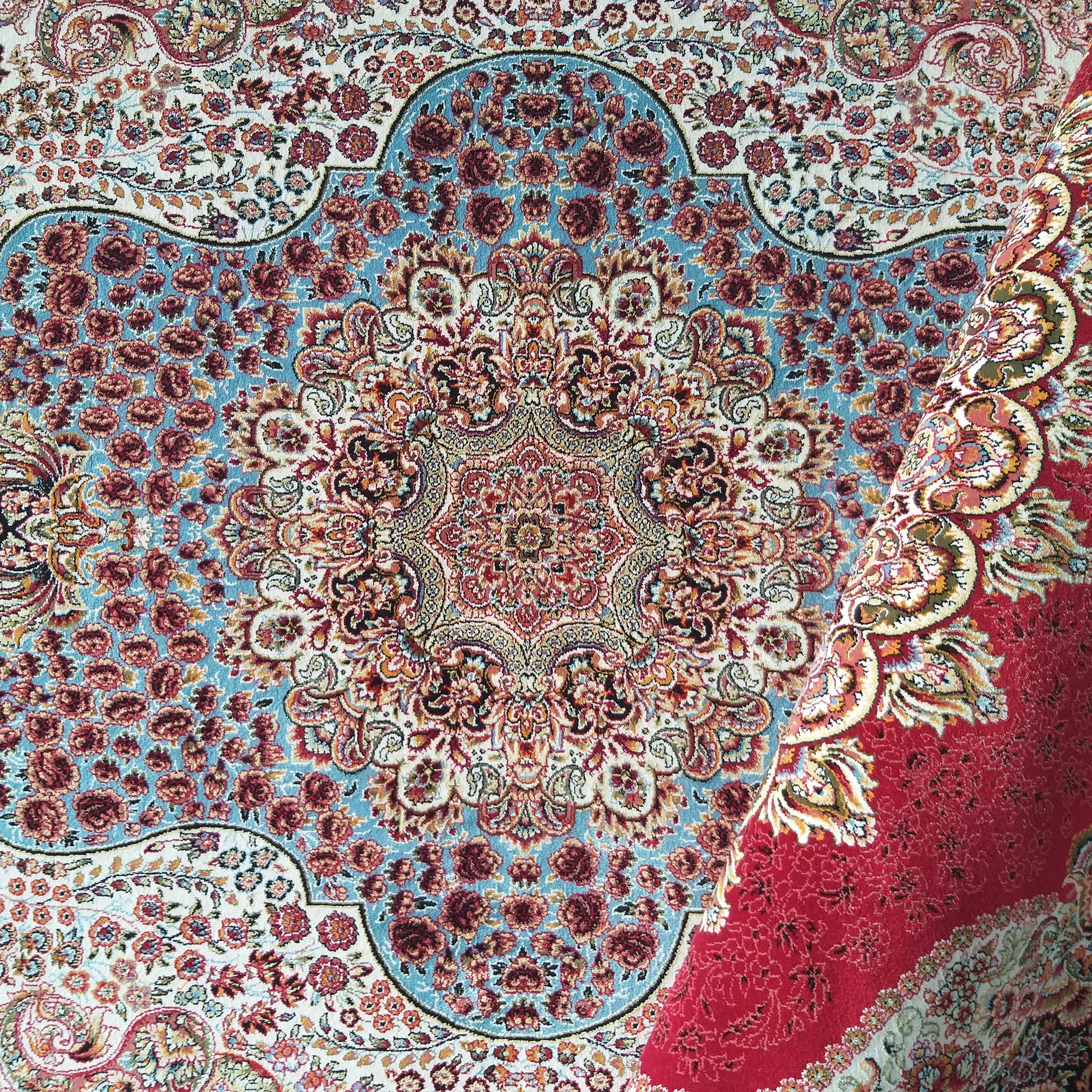 Tapis aux motifs floraux et médaillon central dominés par le bleu, le rouge et le crème, avec une partie roulée
