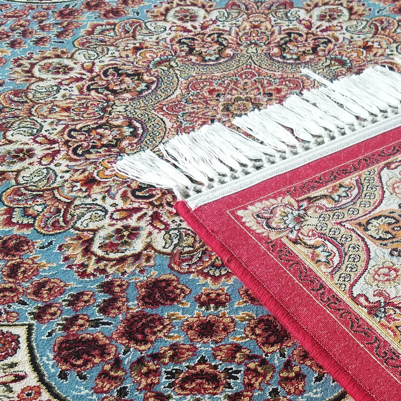 Tapis finement détaillé aux motifs floraux et cachemire, avec des touches de rouge, bleu, beige, or et noir, bordé de franges blanches