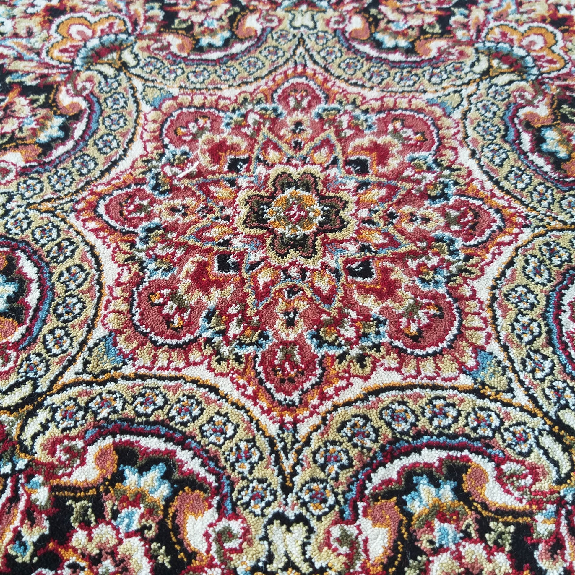 Tapis coloré à motifs ornementaux traditionnels rouges, beiges, dorés, bleus et noirs, avec une texture dense