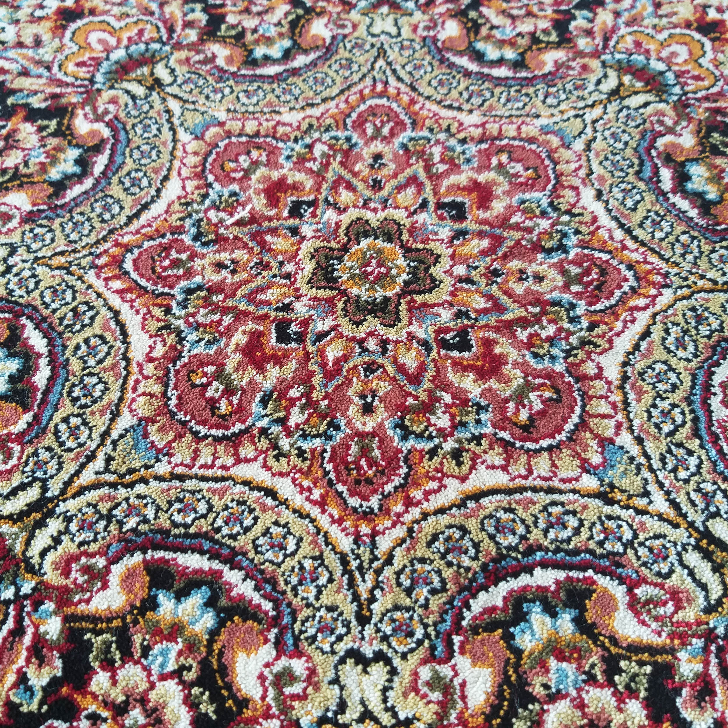 Tapis coloré à motifs ornementaux traditionnels rouges, beiges, dorés, bleus et noirs, avec une texture dense