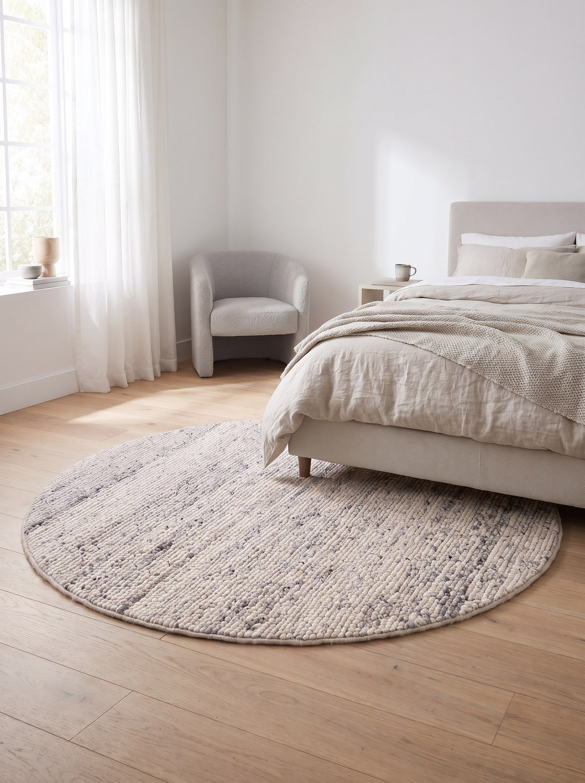 Wollteppich rund Kieselgrau - Feltro neben dem Bett im Schlafzimmer einer hellen Neubauwohnung, auf hellem Eichenparkett