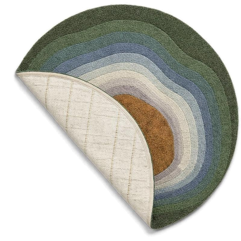 Un coin replié révèle le dos tissé d'un tapis rond en laine tuftée aux bandes vertes et bleues