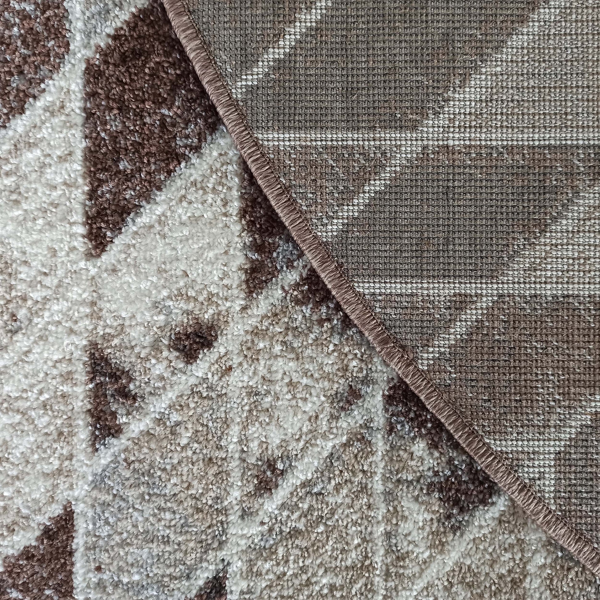 Gros plan sur un tapis texturé marron, beige et blanc, montrant le dessus moelleux et le dessous tissé avec bordure surjetée