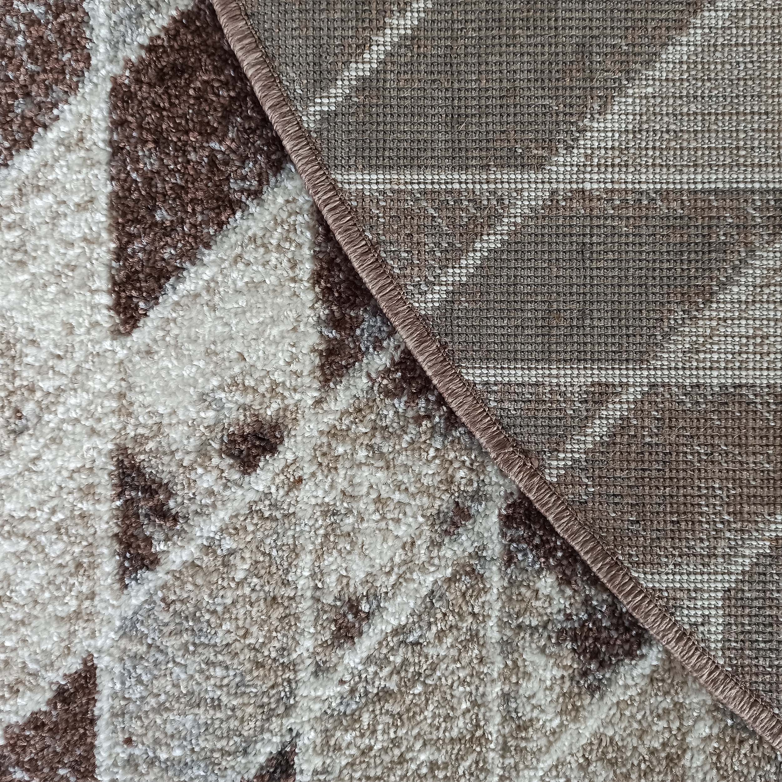 Gros plan sur un tapis texturé marron, beige et blanc, montrant le dessus moelleux et le dessous tissé avec bordure surjetée