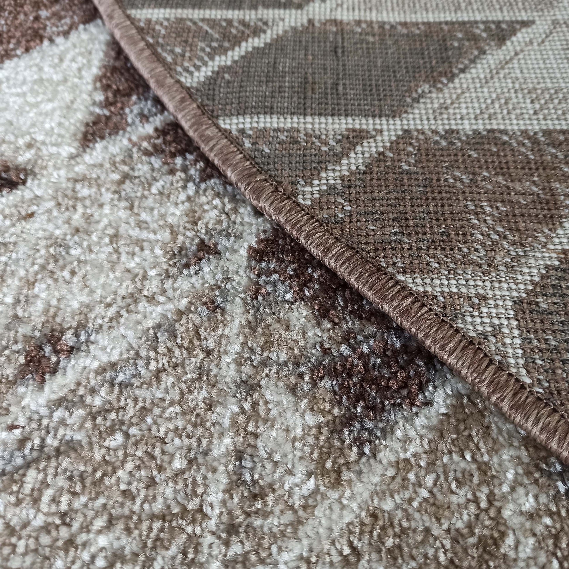Un tapis texturé alliant des poils longs beige et marron à une partie tissée à motifs géométriques marron et beige, séparées par une bordure marron cousue