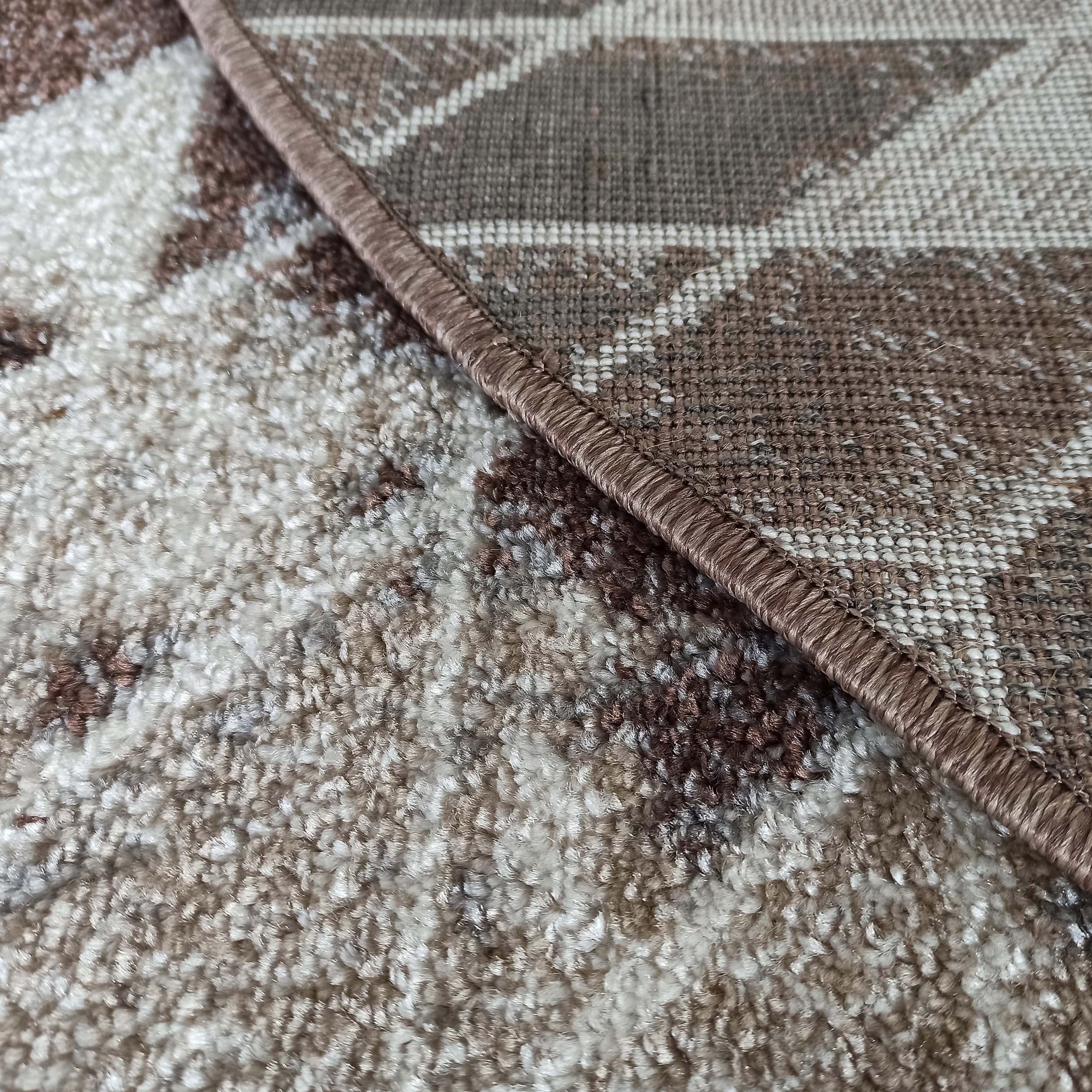 Un tapis texturé alliant des poils longs beige et marron à une partie tissée à motifs géométriques marron et beige, séparées par une bordure marron cousue