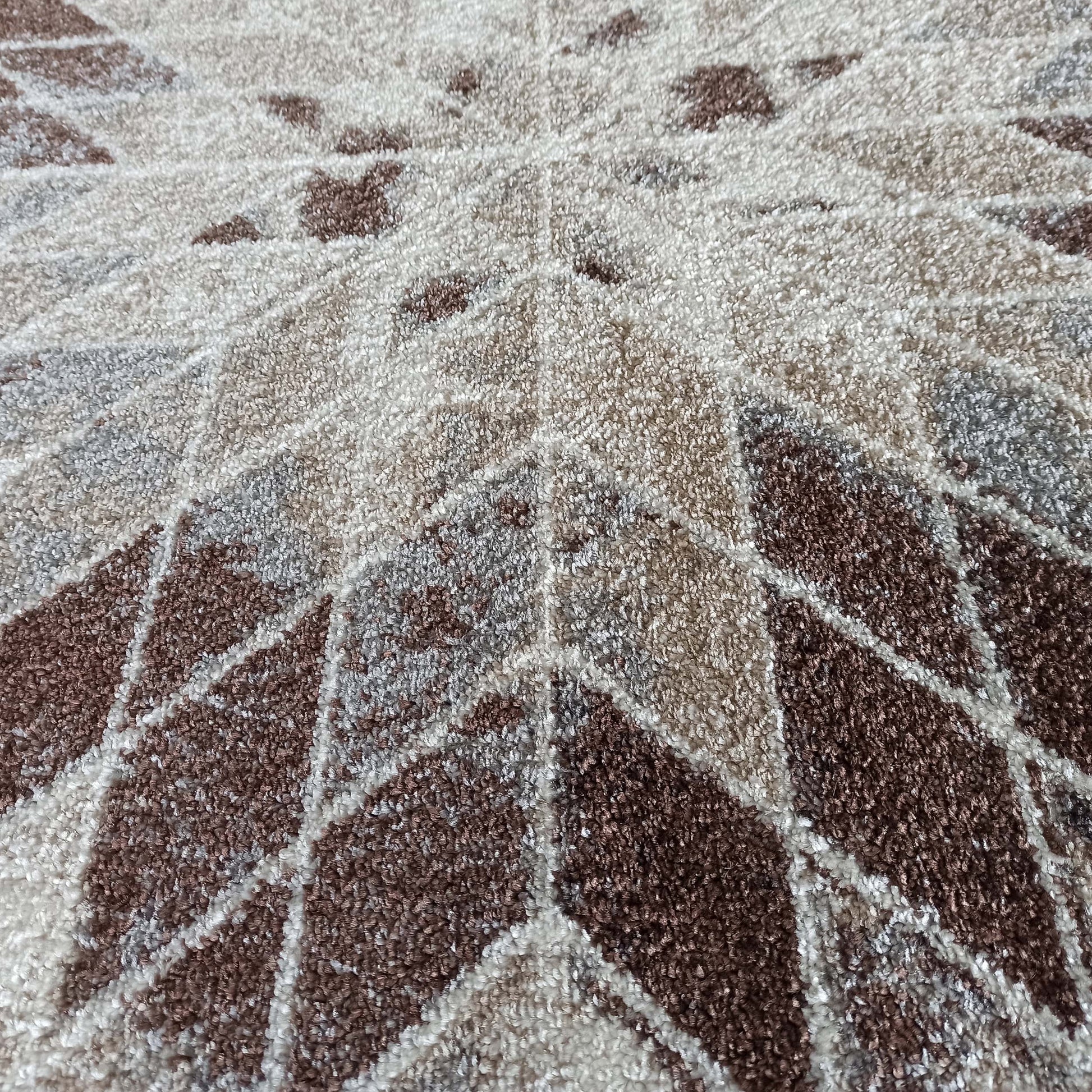 Tapis à poils épais affichant un motif géométrique radial de losanges et triangles en marron, beige et blanc crème