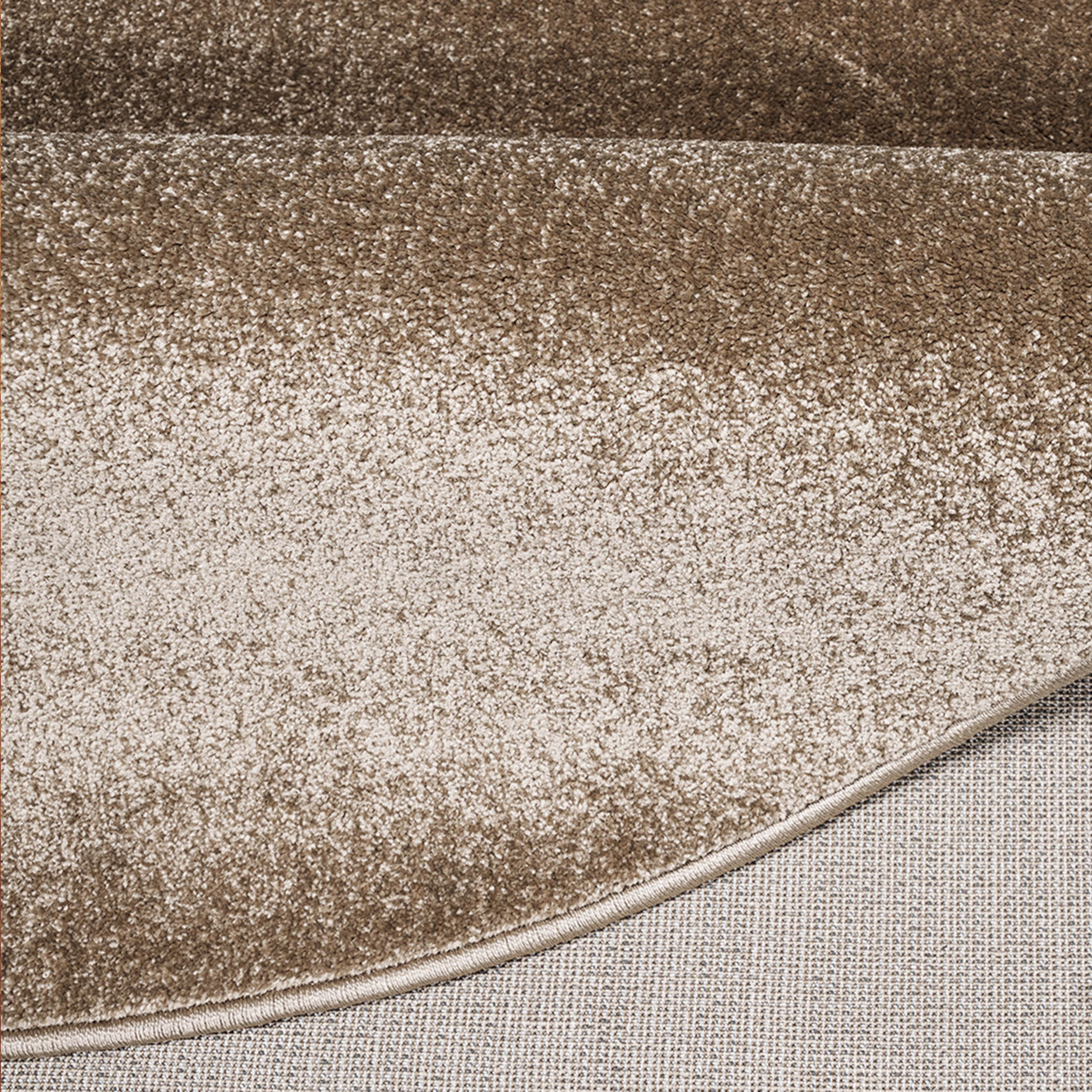 Tapis beige et marron clair à texture douce et mouchetée, montrant son bord ourlé et son envers tissé