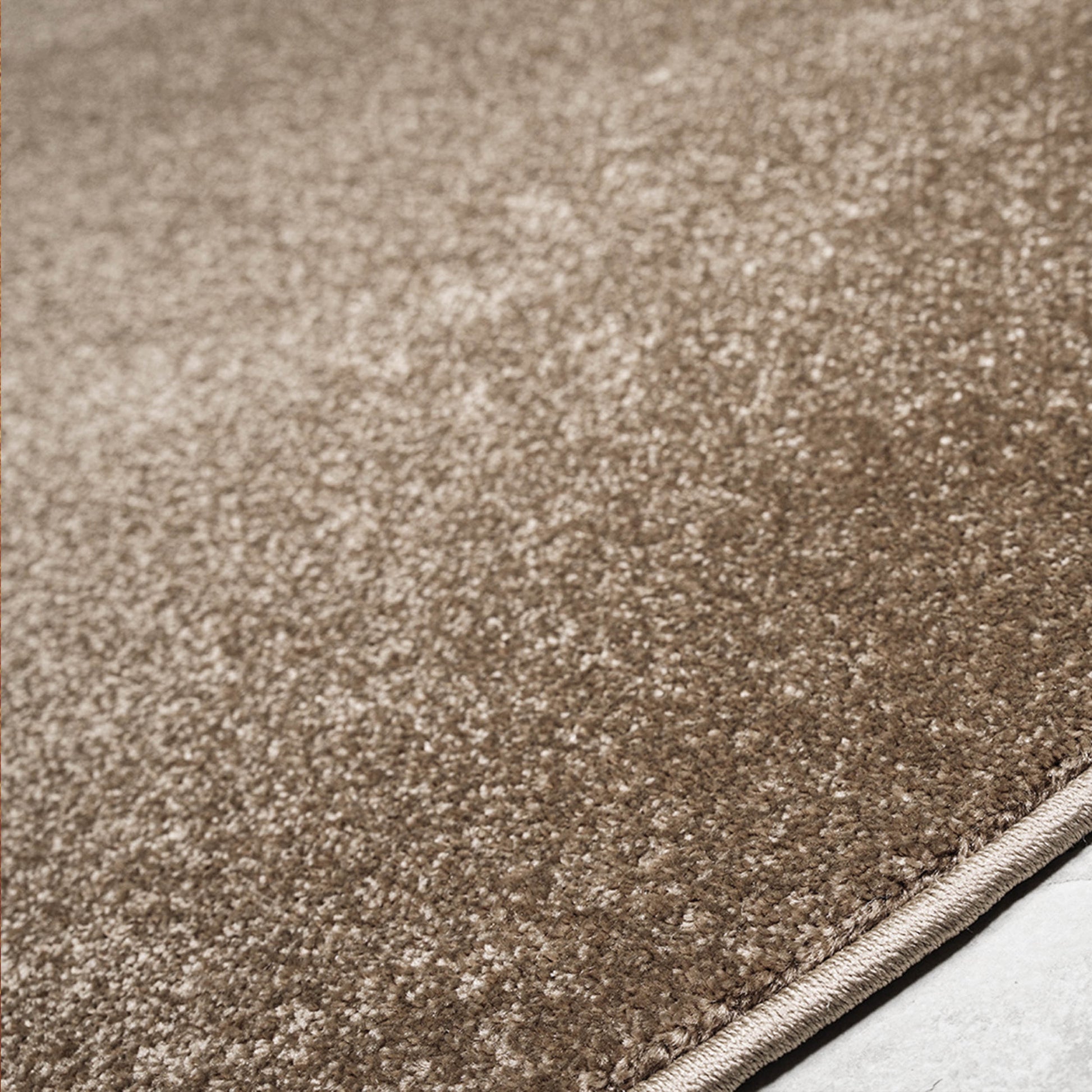 Tapis moelleux aux fibres mélangées marron et beige clair, présentant un aspect chiné et un bord surpiqué