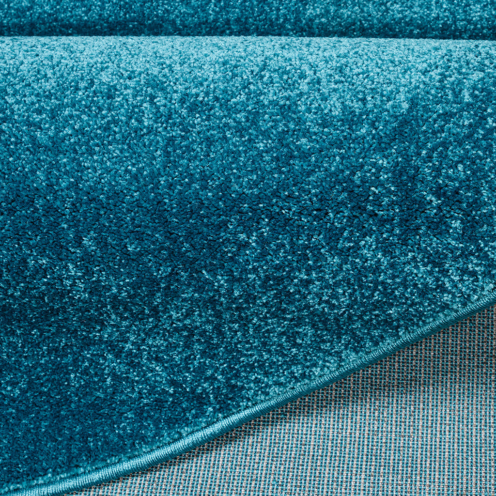 Tapis doux bleu canard avec une bordure visible et le revers tissé gris clair exposé par un pli