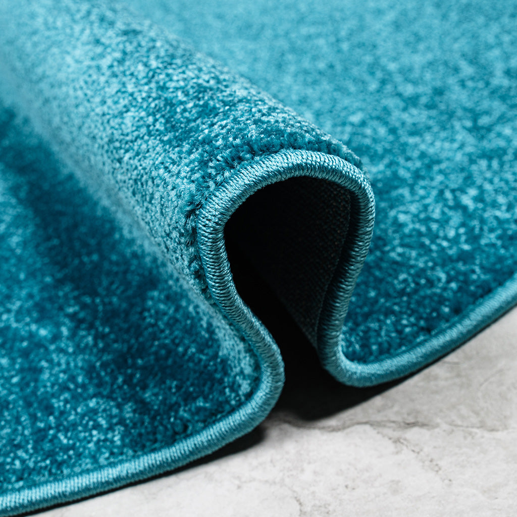 Gros plan d'un tapis bleu sarcelle à la texture douce et mouchetée, une partie est roulée, sur un sol gris clair