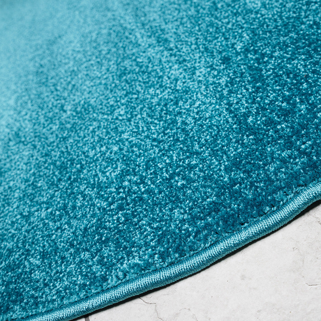 Tapis bleu turquoise uni, vu en gros plan, montrant une texture douce et dense avec un bord apparent