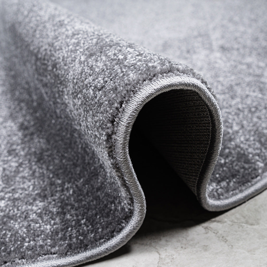Gros plan d'un tapis gris aux fibres douces et mouchetées, roulé sur un côté avec une bordure claire
