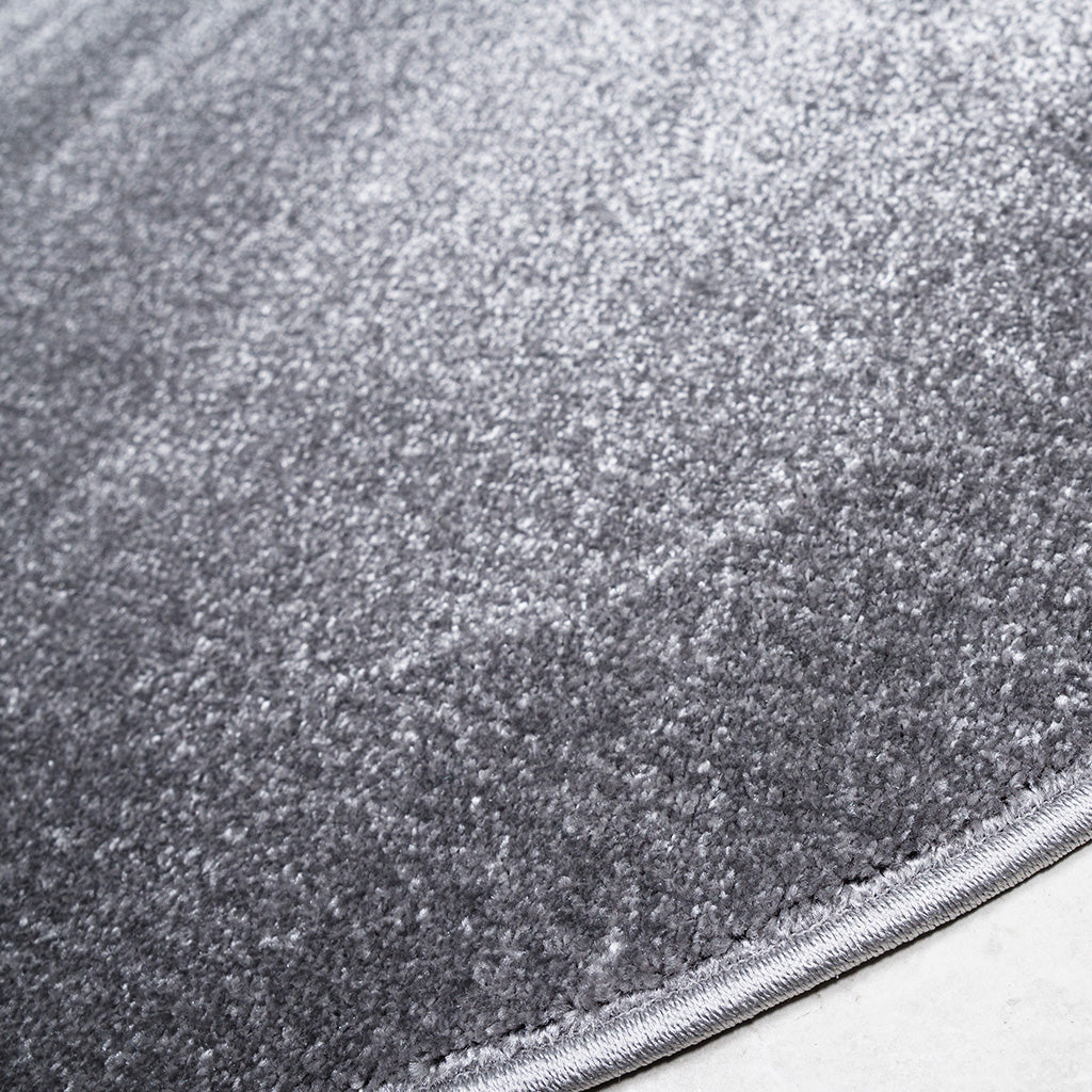Tapis gris texturé à poils courts, présentant des nuances claires et foncées sur sa surface douce, avec une bordure nette