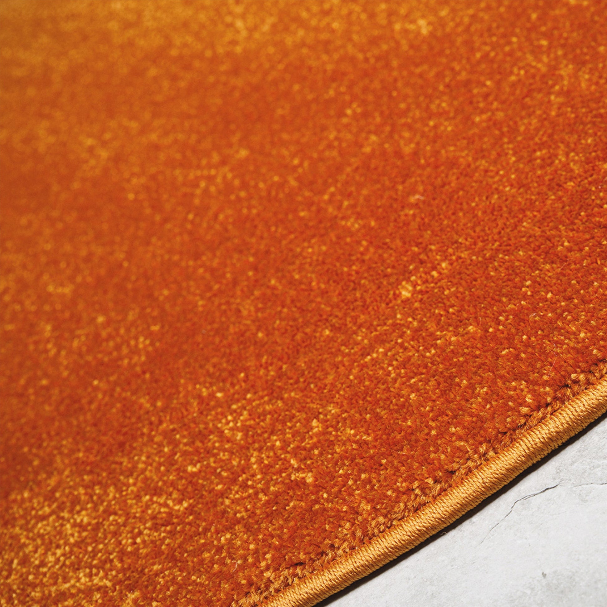 Un tapis couleur rouille aux nuances dorées, avec une texture dense et moelleuse et une bordure cousue sur le côté