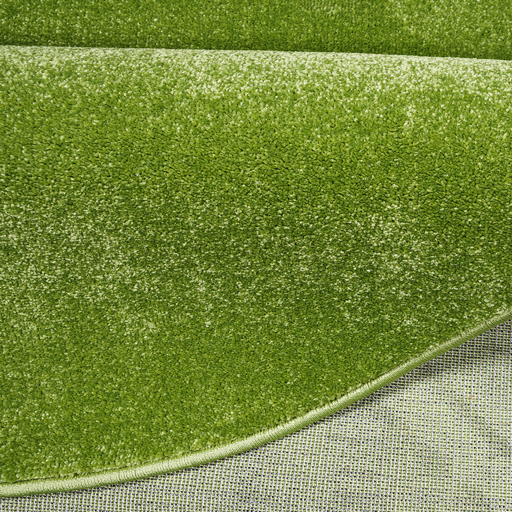Tapis vert pomme moelleux aux fibres denses, parsemé de taches claires, avec son bord ourlé et son envers visible