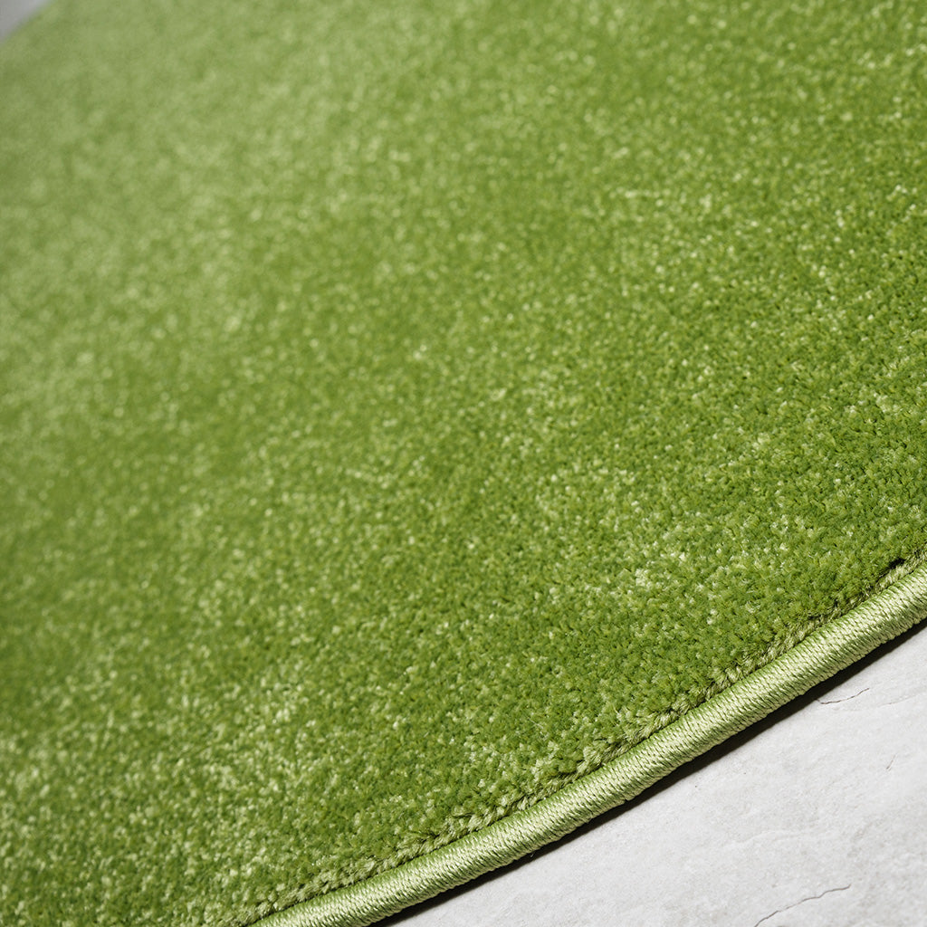 Tapis vert vif à poils courts et épais, avec un bord cousu, posé sur un sol en pierre claire