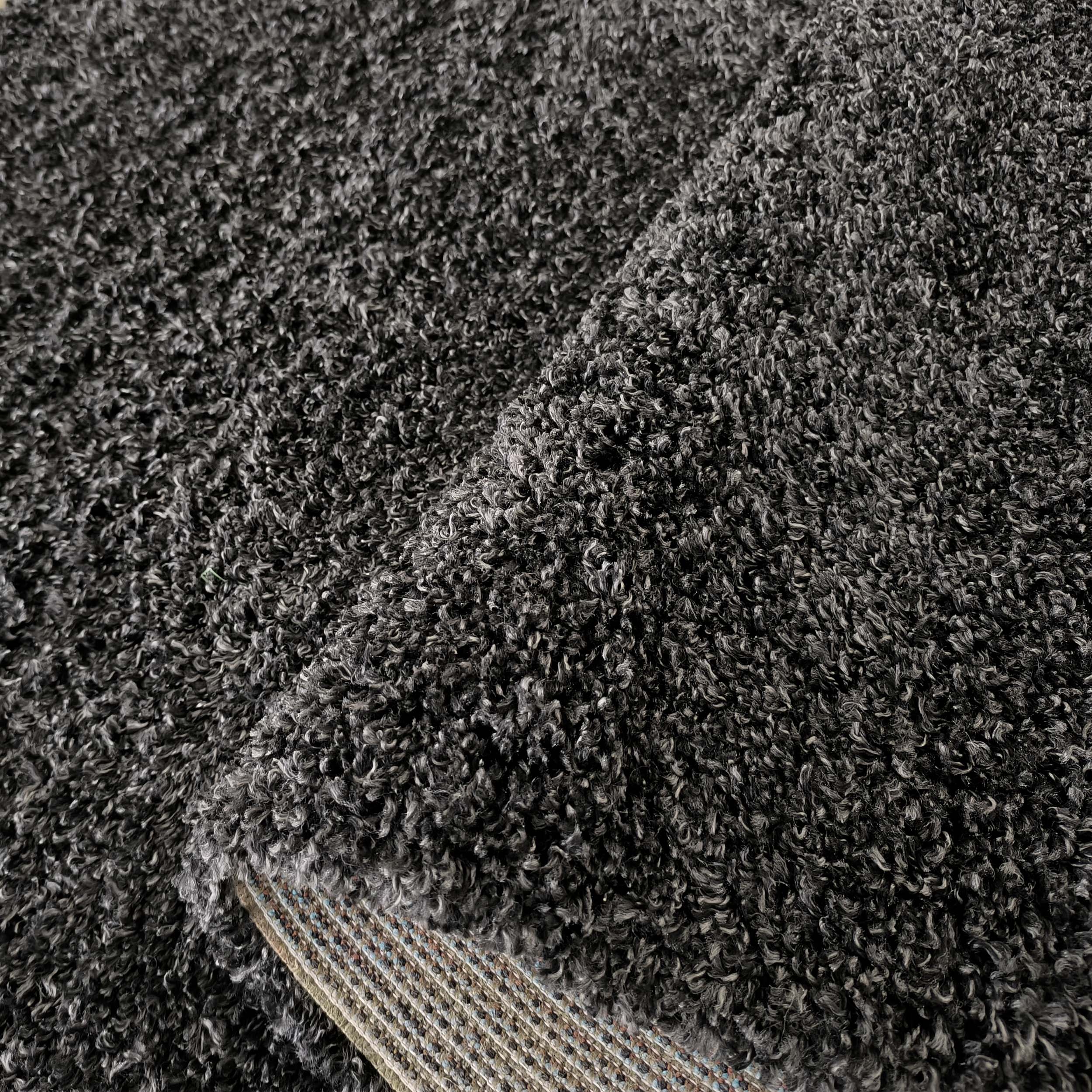 Tapis shaggy gris anthracite avec des mèches plus claires. Un pli révèle son envers tissé à motifs