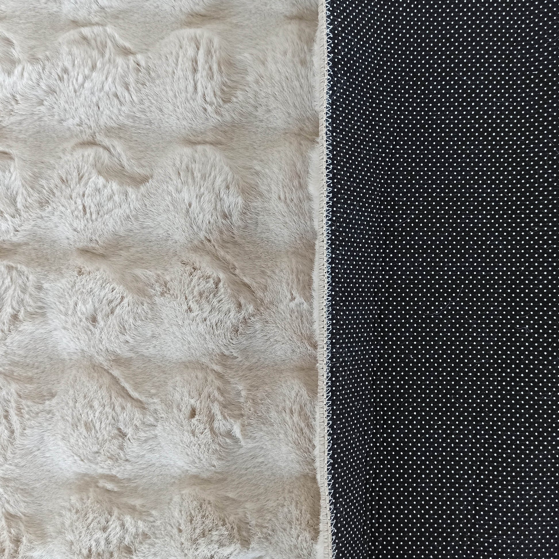 Tapis doux et moelleux beige clair avec une texture évoquant la fourrure, bordé d'un envers noir antidérapant à pois blancs
