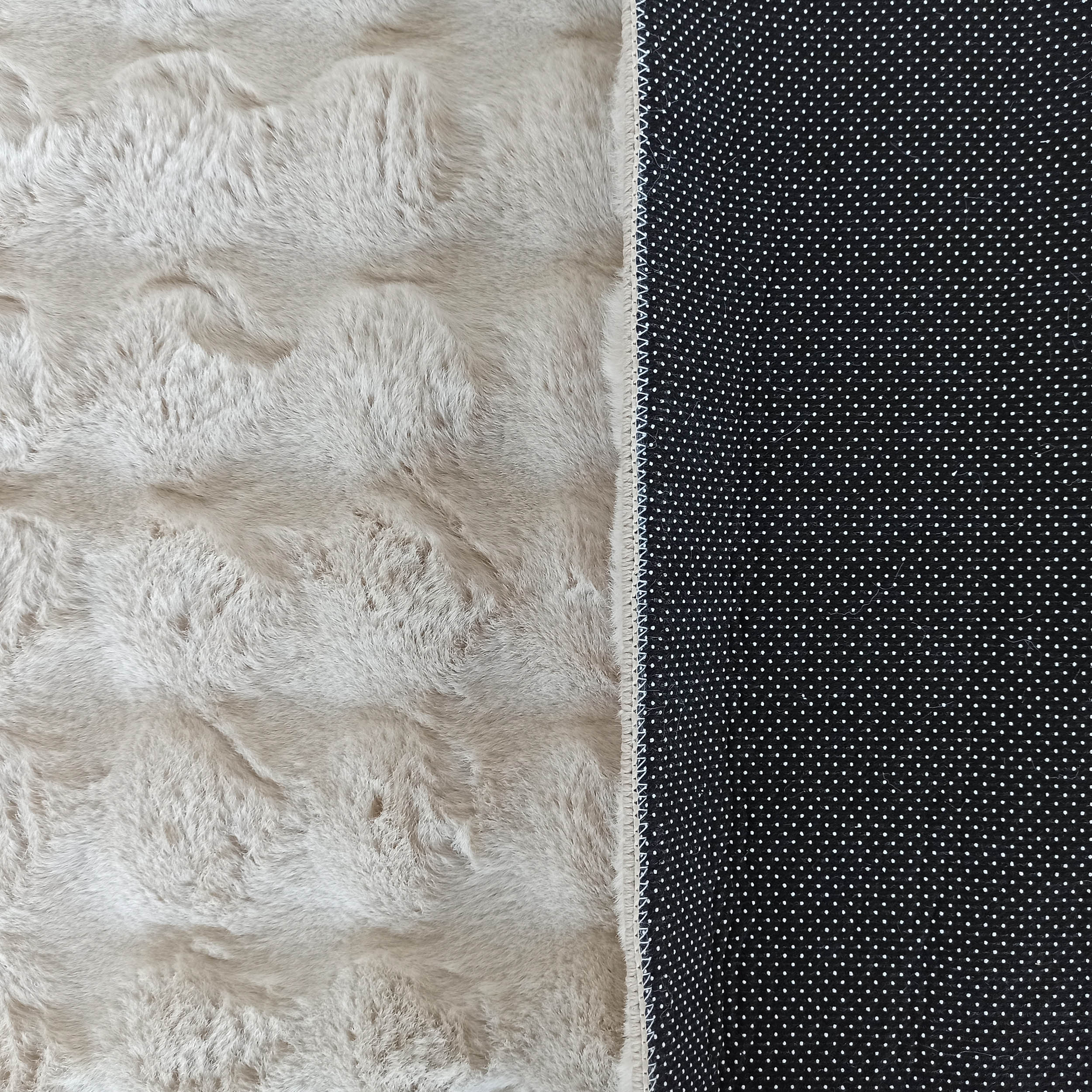 Tapis doux et moelleux beige clair avec une texture évoquant la fourrure, bordé d'un envers noir antidérapant à pois blancs