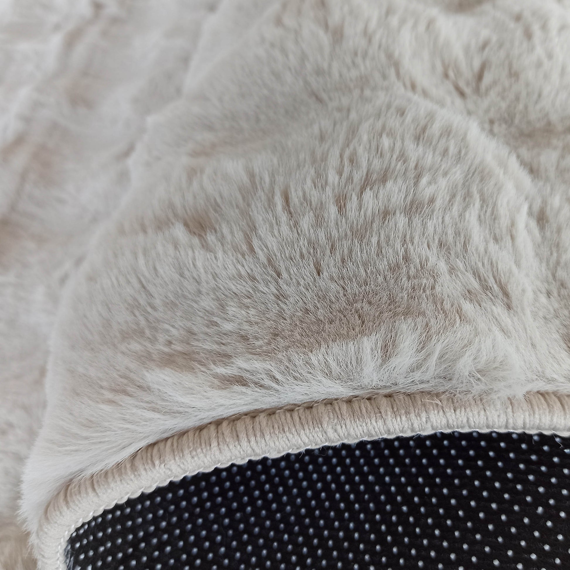 Tapis doux et moelleux aux poils longs de couleur beige clair, bordé d'une surpiqûre et révélant un dessous noir à picots anti-dérapants
