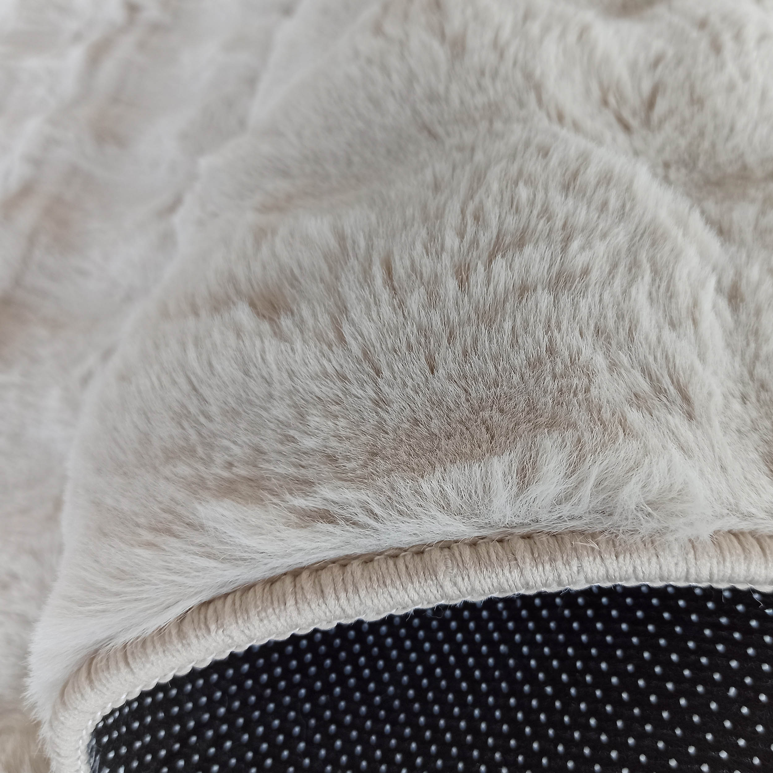 Tapis doux et moelleux aux poils longs de couleur beige clair, bordé d'une surpiqûre et révélant un dessous noir à picots anti-dérapants