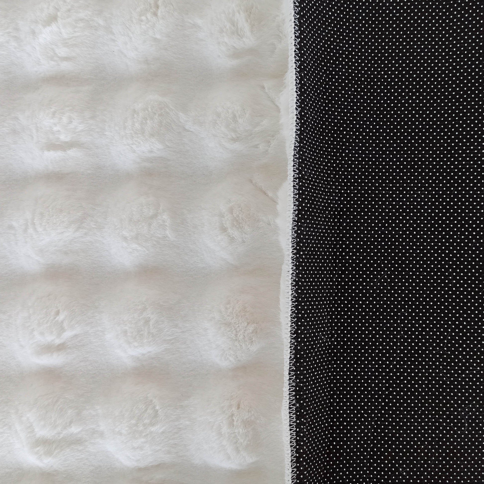 Tapis bicolore avec un côté blanc duveteux à texture fourrure et un revers noir antidérapant à pois blancs
