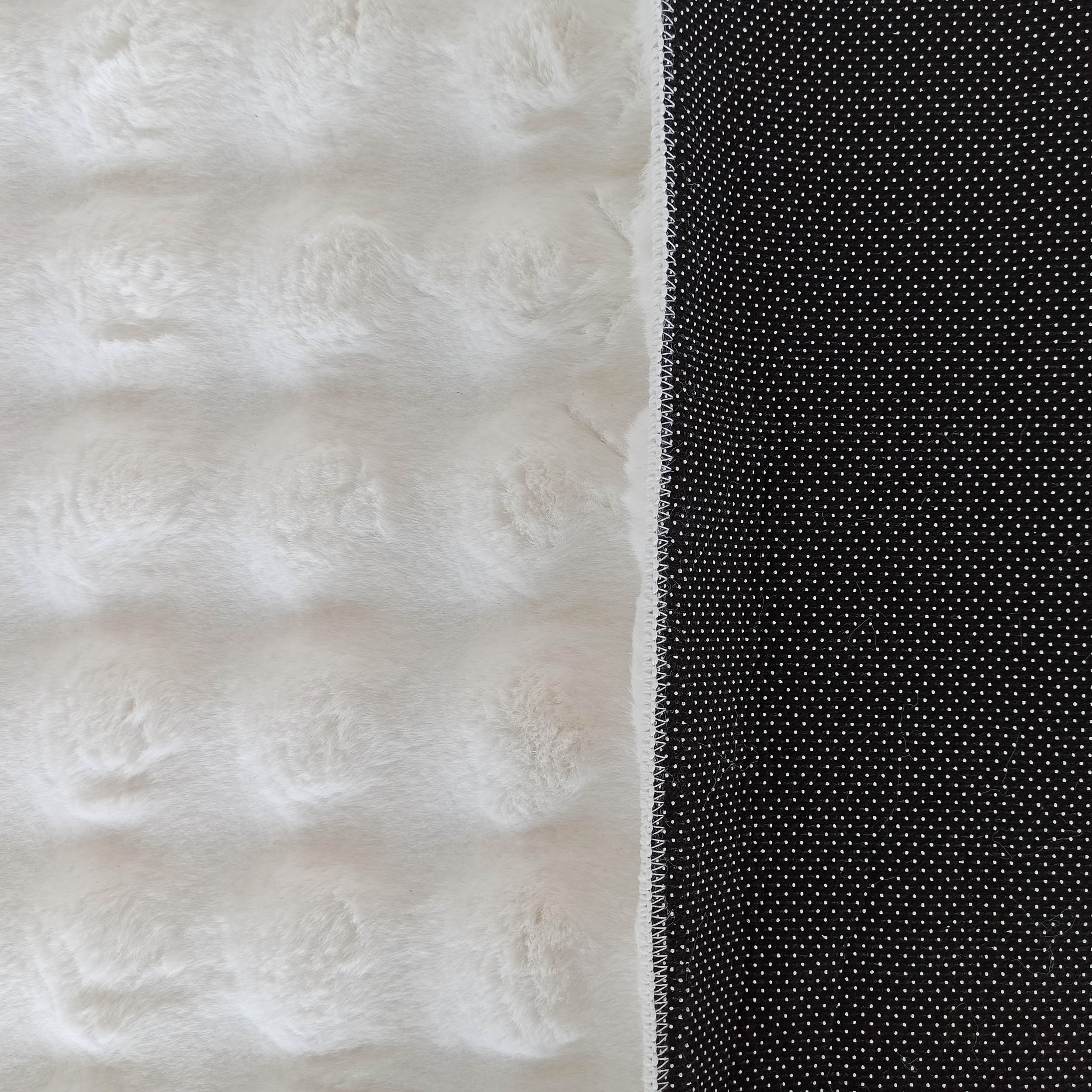 Tapis bicolore avec un côté blanc duveteux à texture fourrure et un revers noir antidérapant à pois blancs