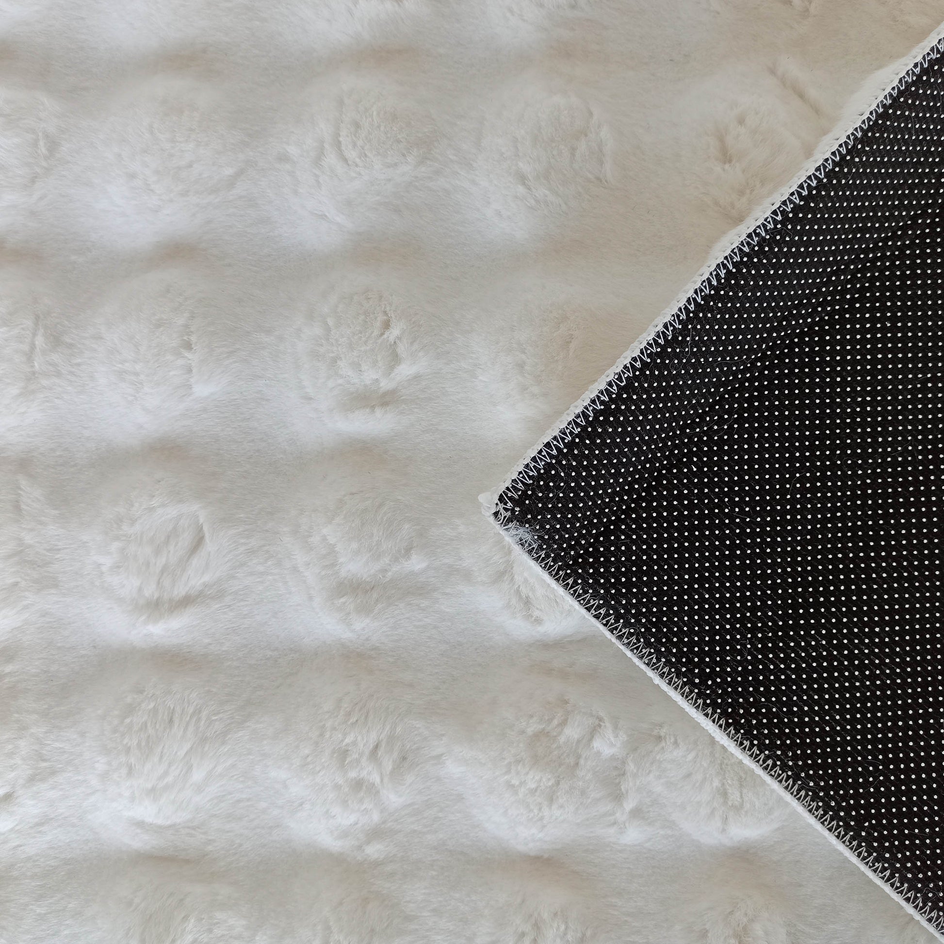 Tapis moelleux blanc cassé à poils longs, un coin replié révèle le dessous noir à motifs de pois blancs