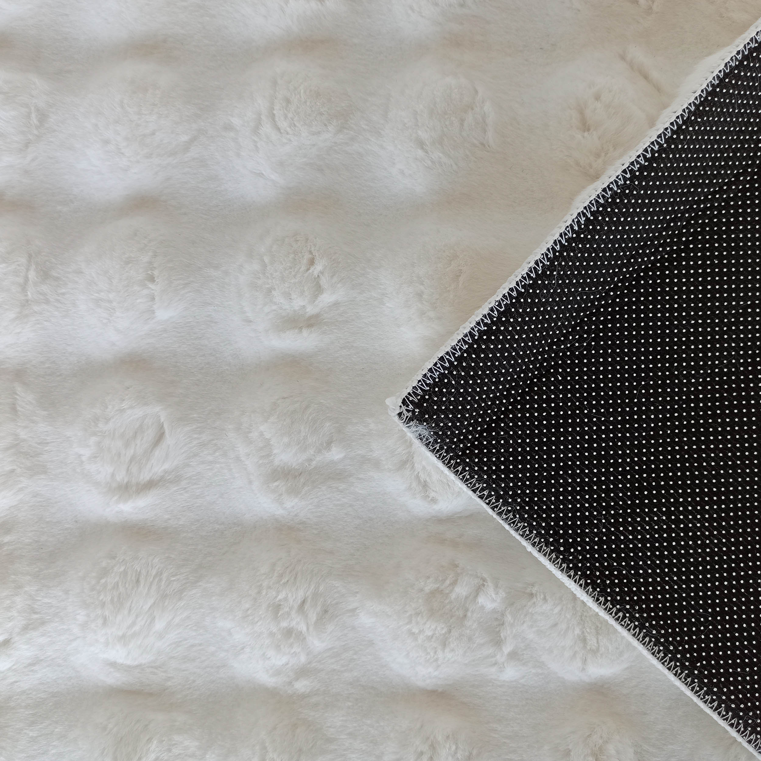 Tapis moelleux blanc cassé à poils longs, un coin replié révèle le dessous noir à motifs de pois blancs
