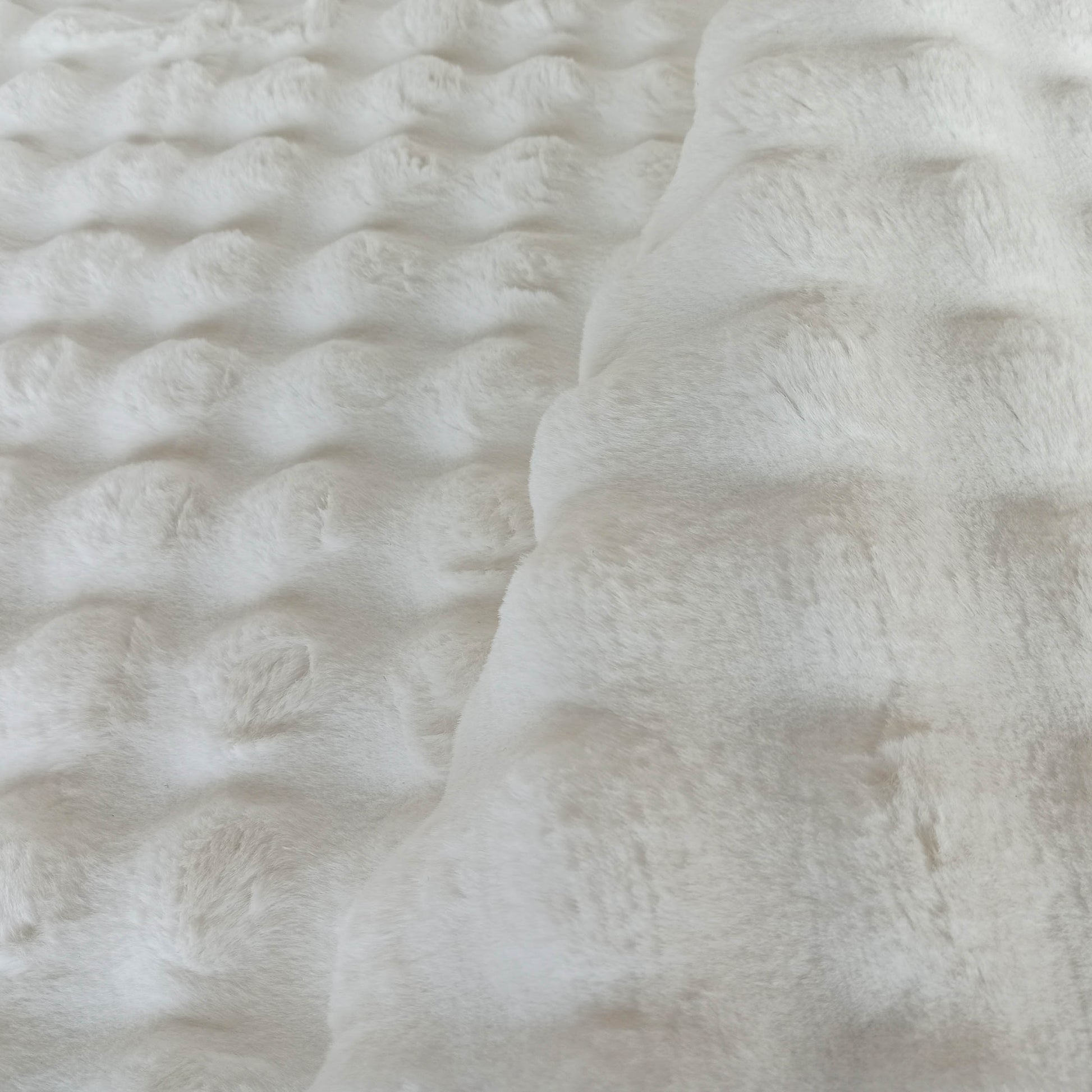Tapis blanc cassé à la texture moelleuse et douce, présentant des motifs circulaires en relief sur une partie