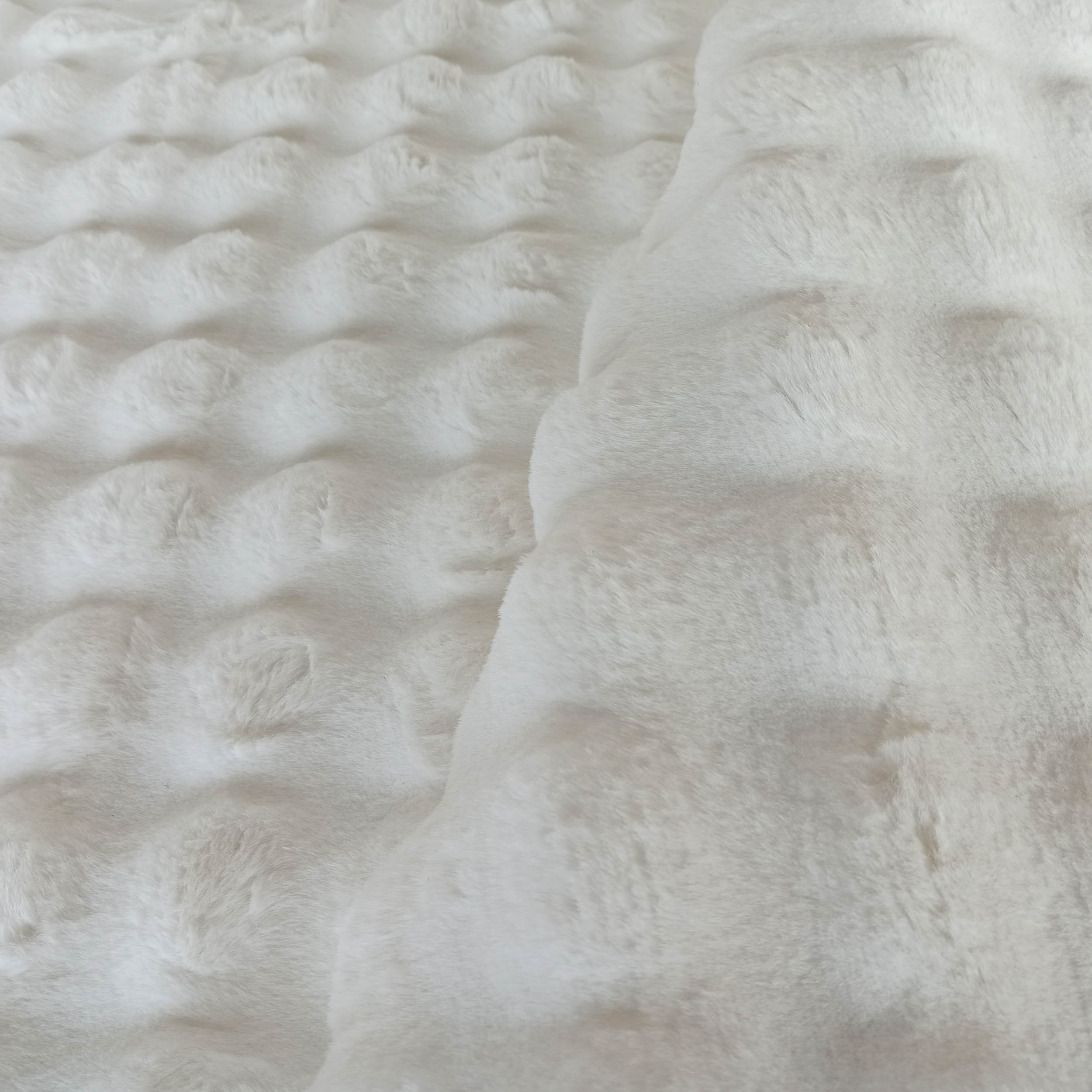 Tapis blanc cassé à la texture moelleuse et douce, présentant des motifs circulaires en relief sur une partie