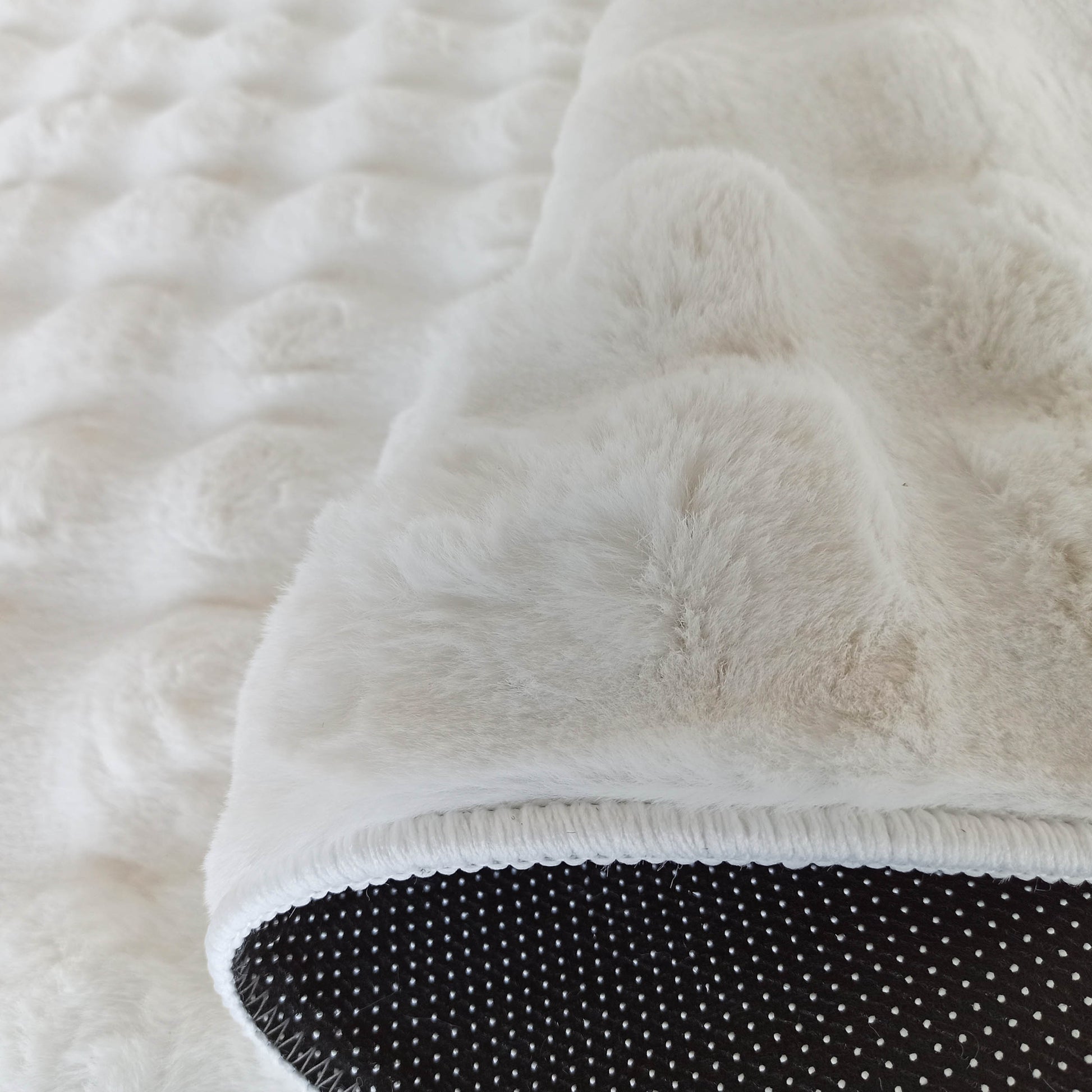 Tapis blanc doux et duveteux, montrant son envers noir avec un motif de pois blancs
