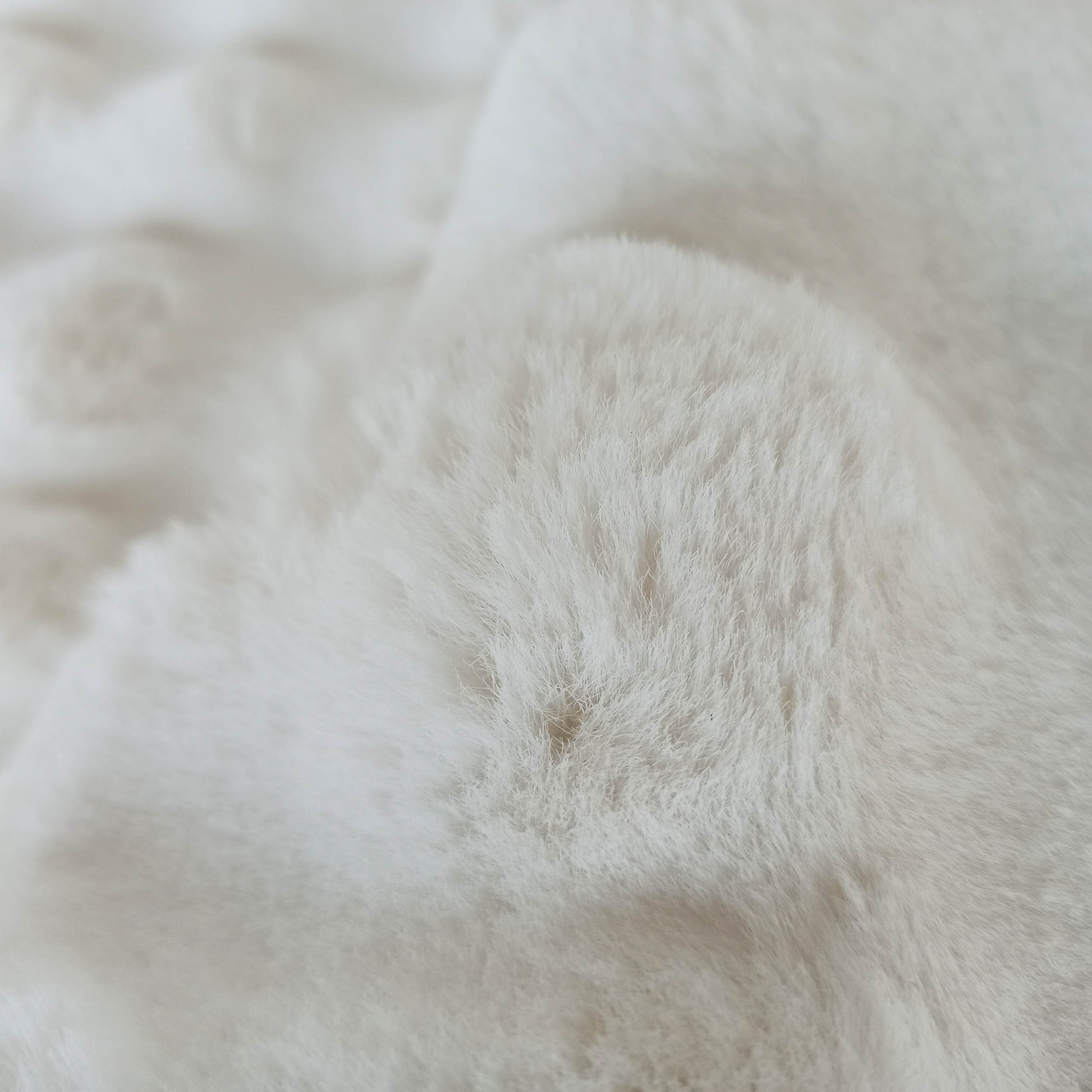 Tapis moelleux blanc cassé à poils longs, dont la texture duveteuse imite la fourrure et présente des ondulations