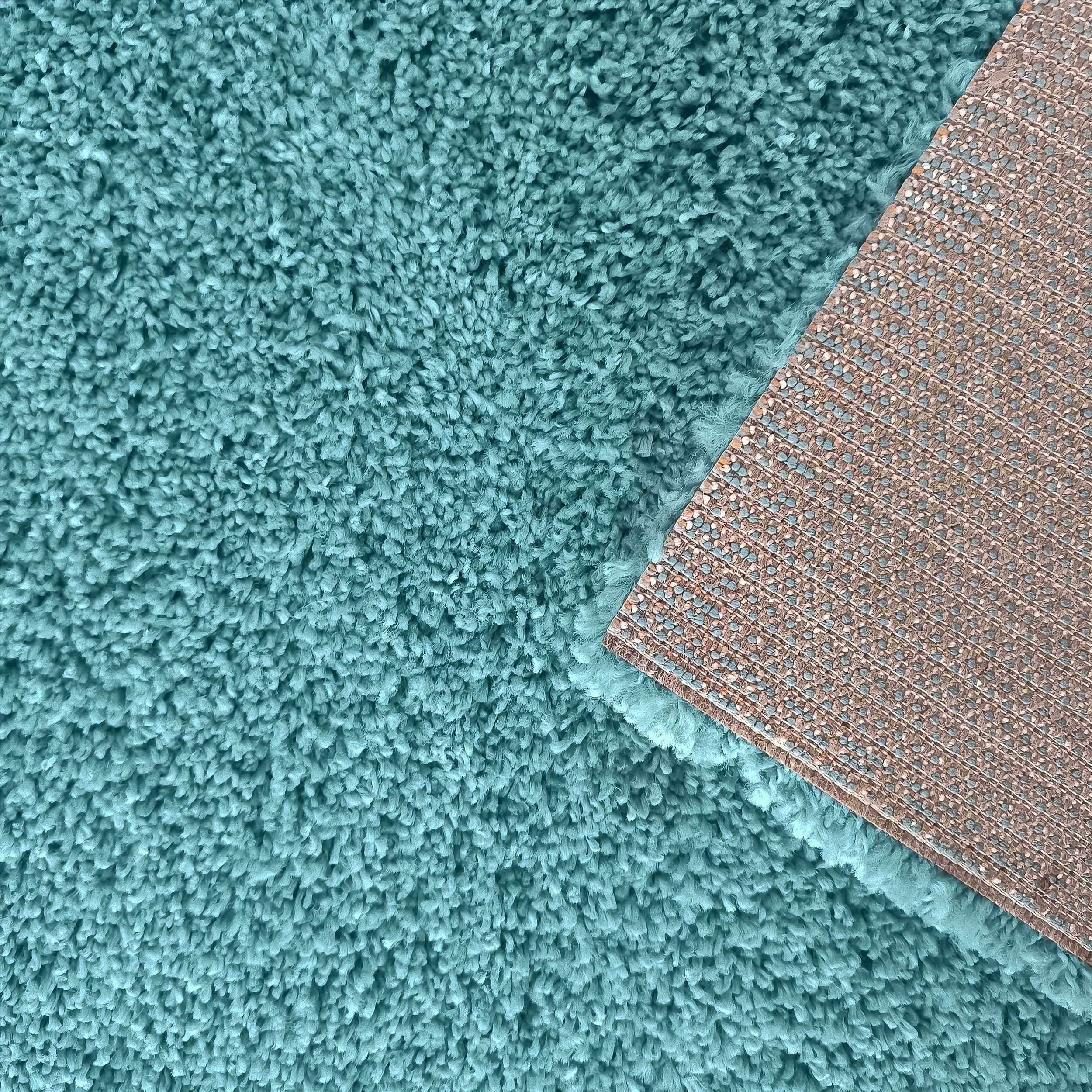 Gros plan sur un tapis turquoise à poils longs, avec un coin relevé montrant son envers tissé beige et bleu