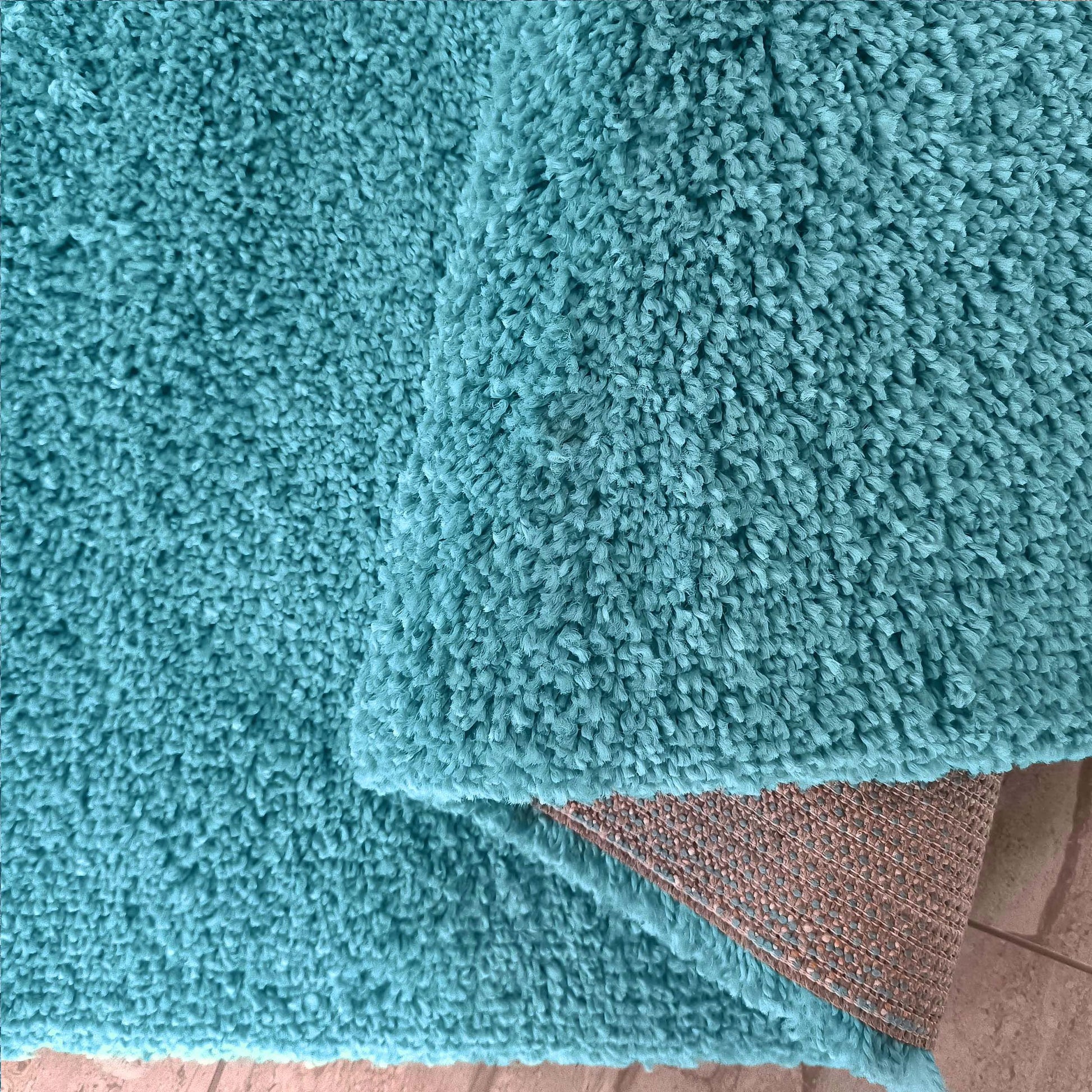 Tapis moelleux turquoise au long poil, avec un coin replié révélant son envers tissé marron clair