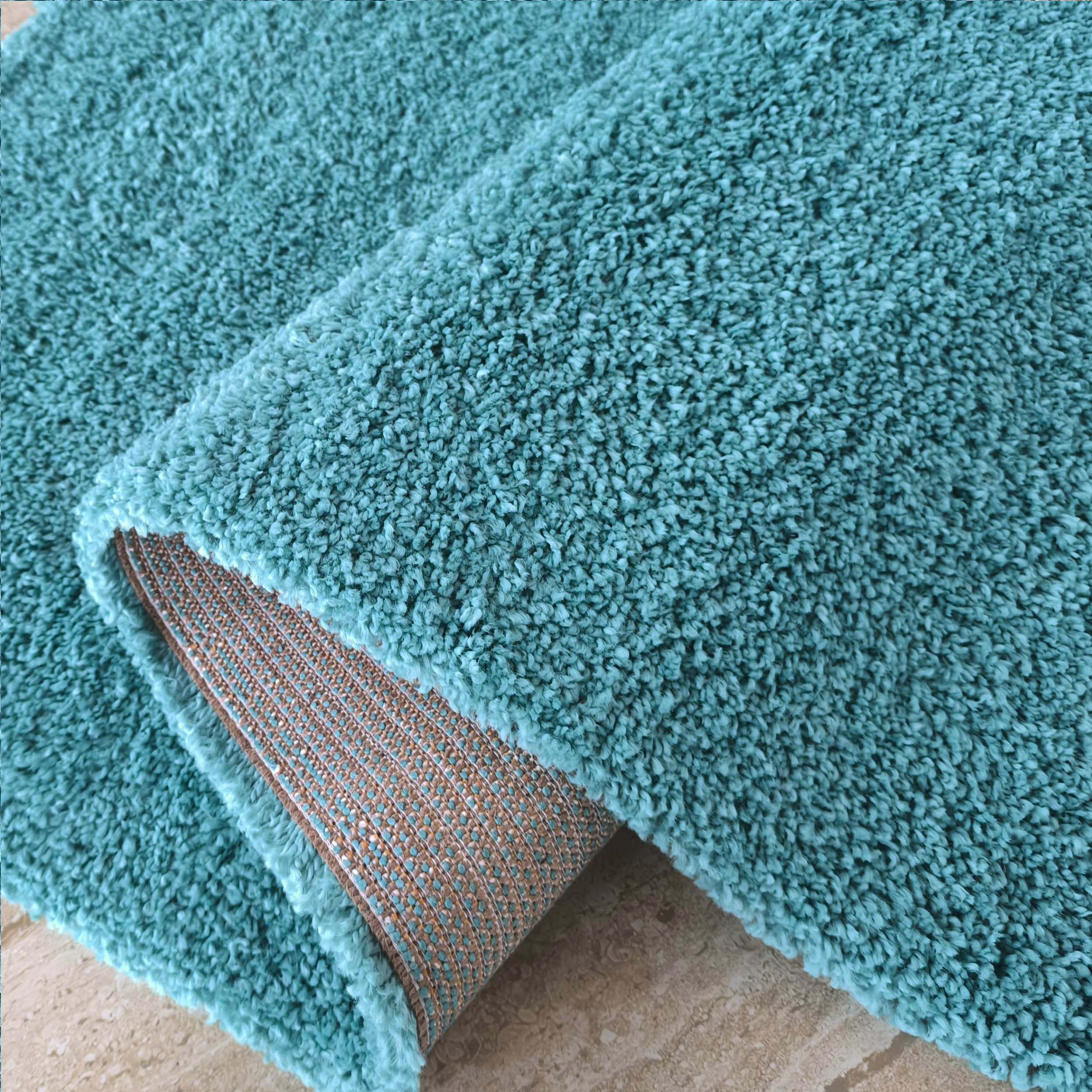 Tapis moelleux bleu turquoise à la texture shag, une partie est enroulée montrant l'envers tissé beige et bleu