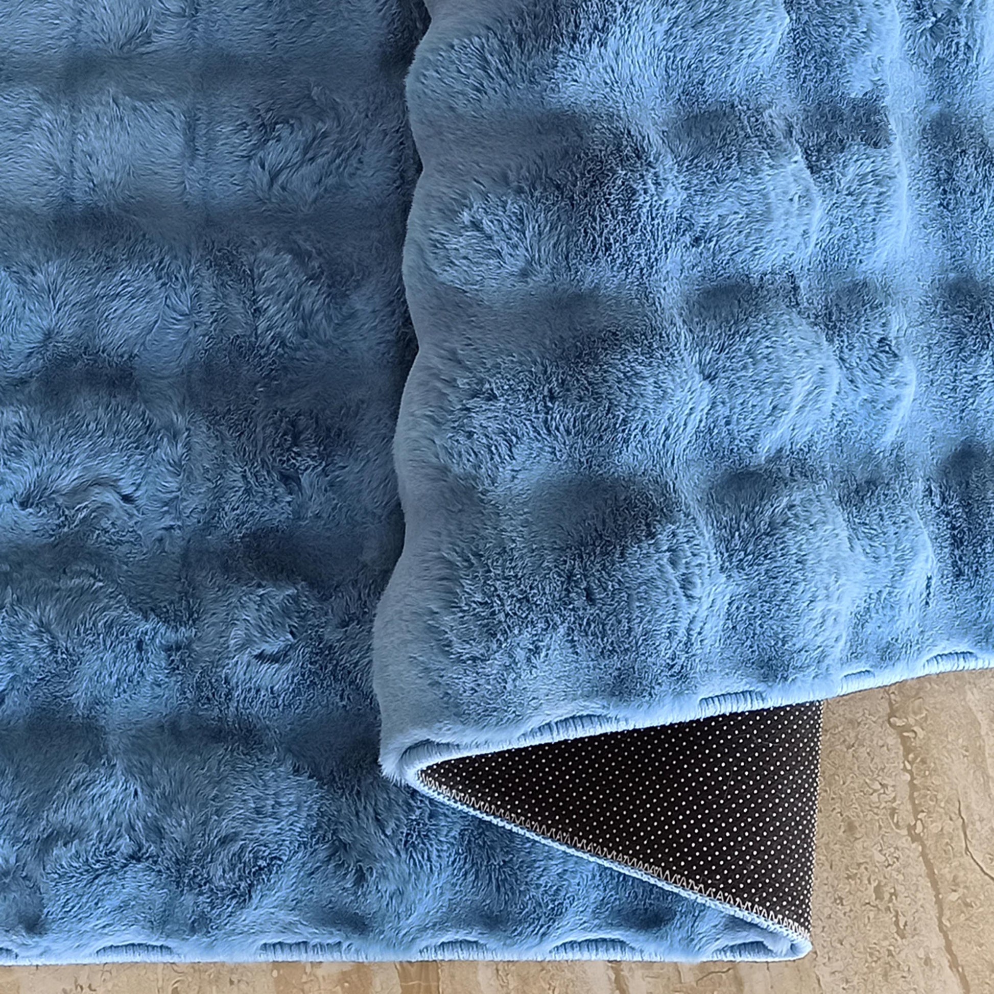 Tapis bleu ciel à texture douce et légèrement ondulée, montrant son envers antidérapant noir à pois sur un sol beige