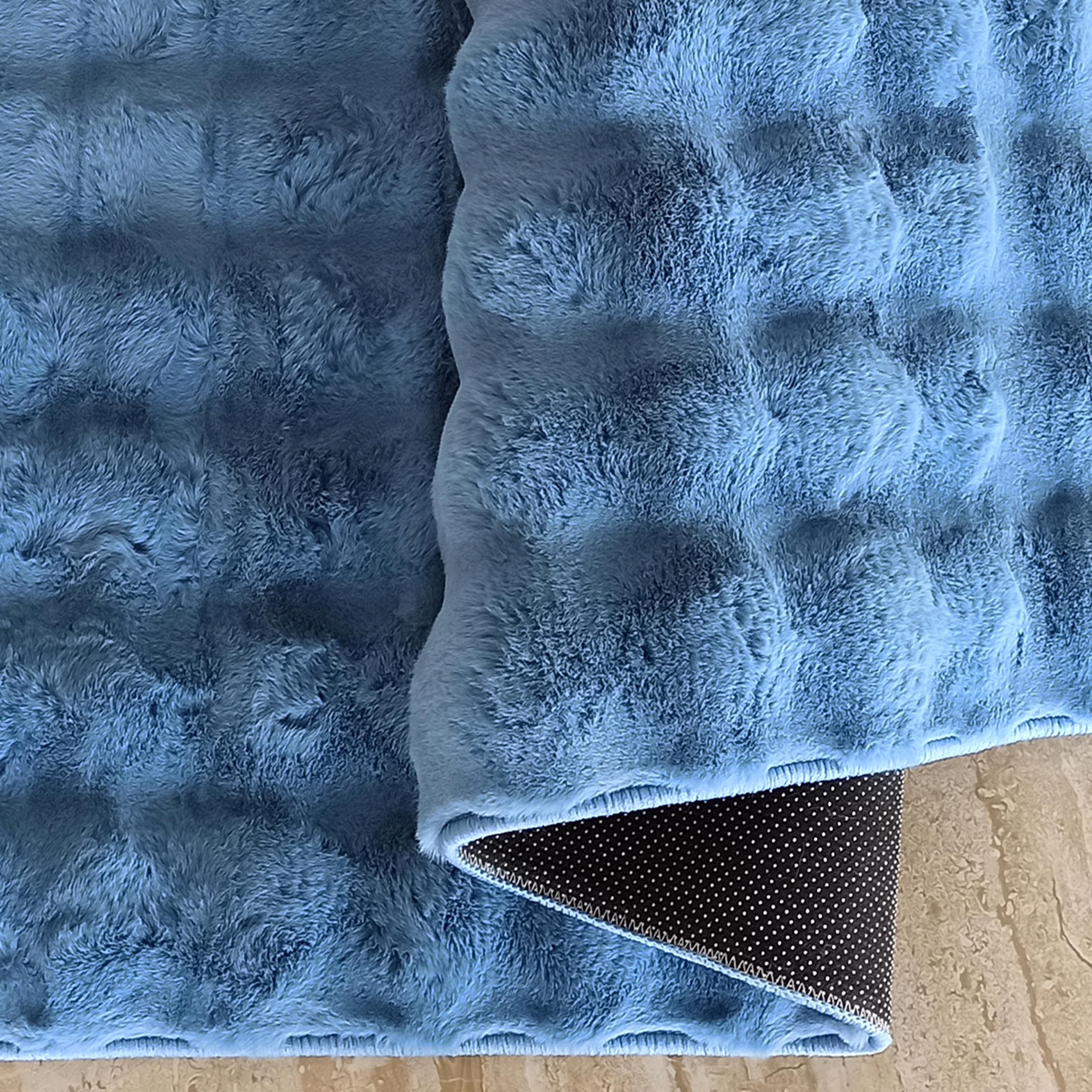 Tapis bleu ciel à texture douce et légèrement ondulée, montrant son envers antidérapant noir à pois sur un sol beige
