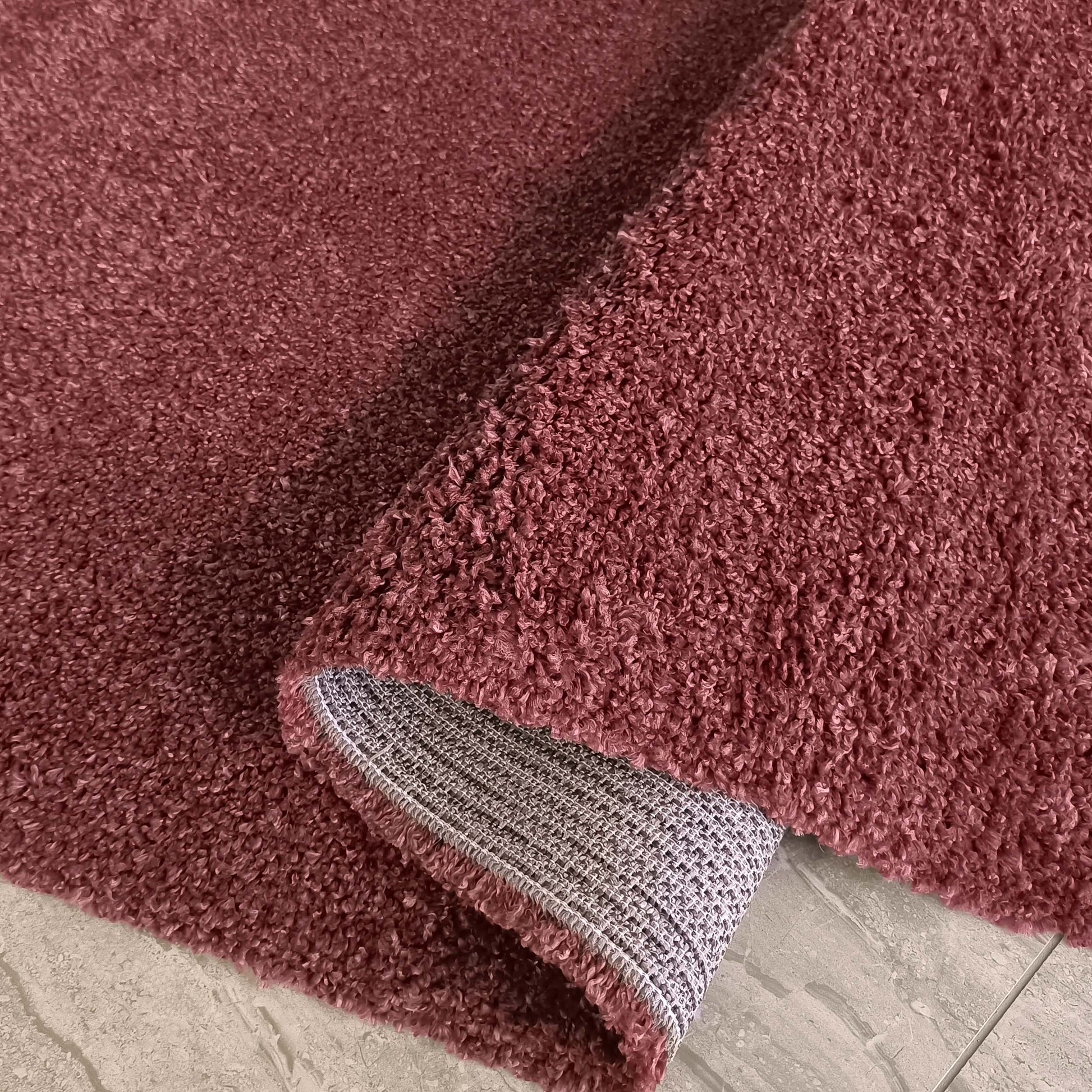 Tapis rose ancien à la texture douce et bouclée, roulé pour révéler son envers tissé sur un carrelage gris
