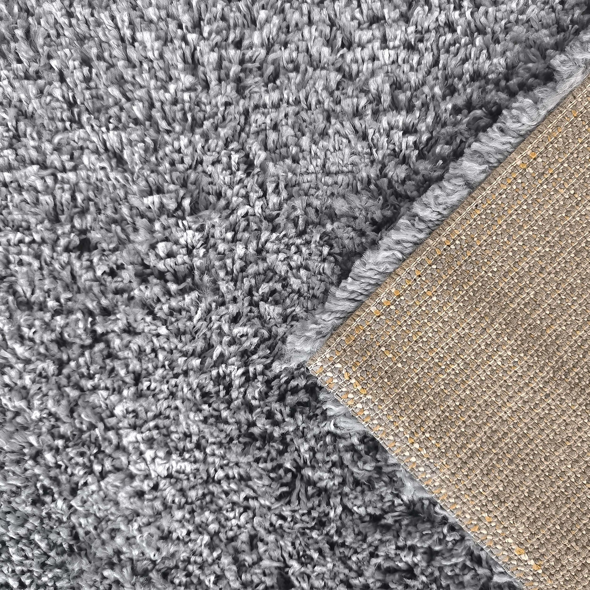 Tapis gris à texture shaggy à poils longs, avec un coin relevé pour révéler son envers beige tissé et texturé