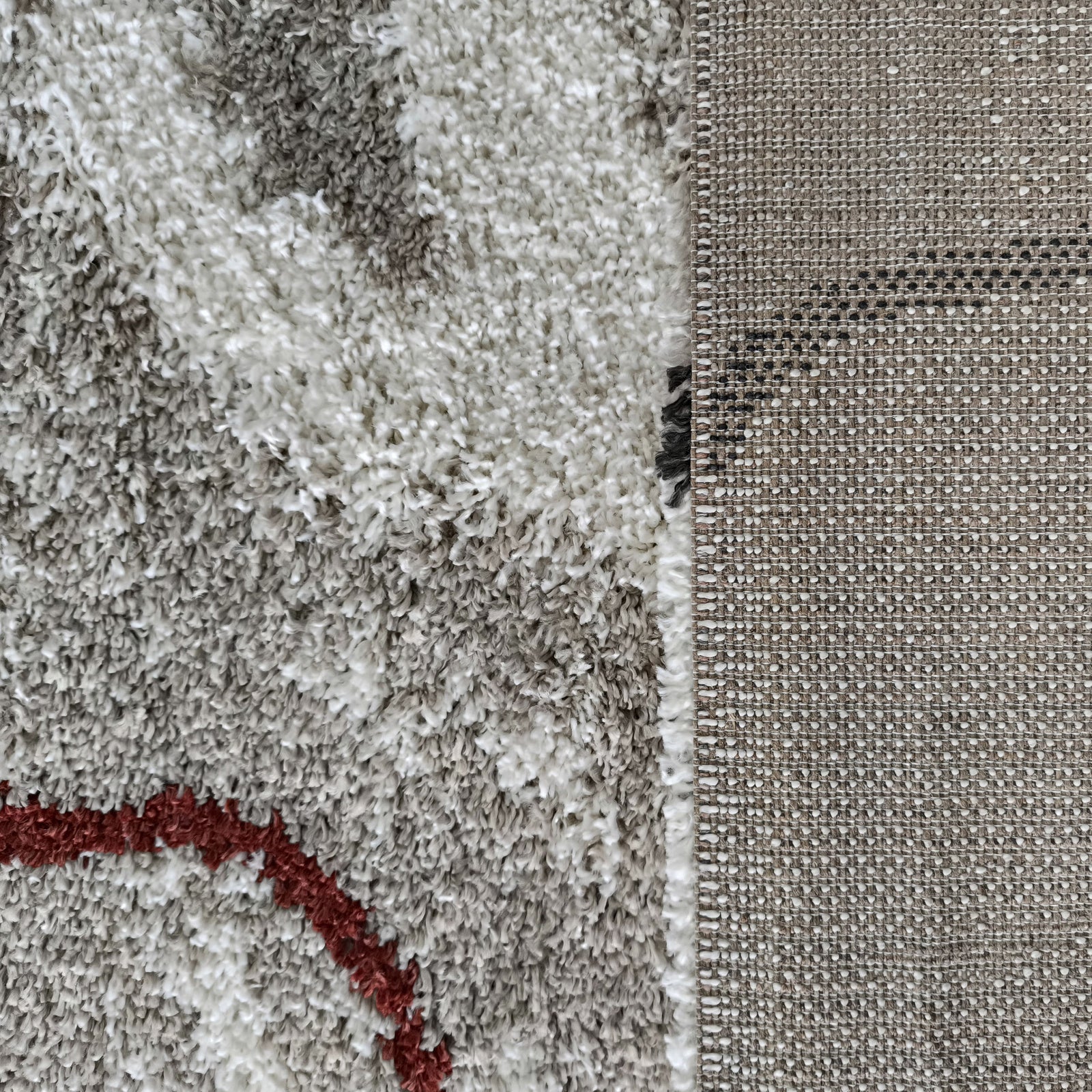 Gros plan d'un tapis à poils longs aux motifs abstraits gris, blanc et rouge, et de son envers tissé beige et blanc