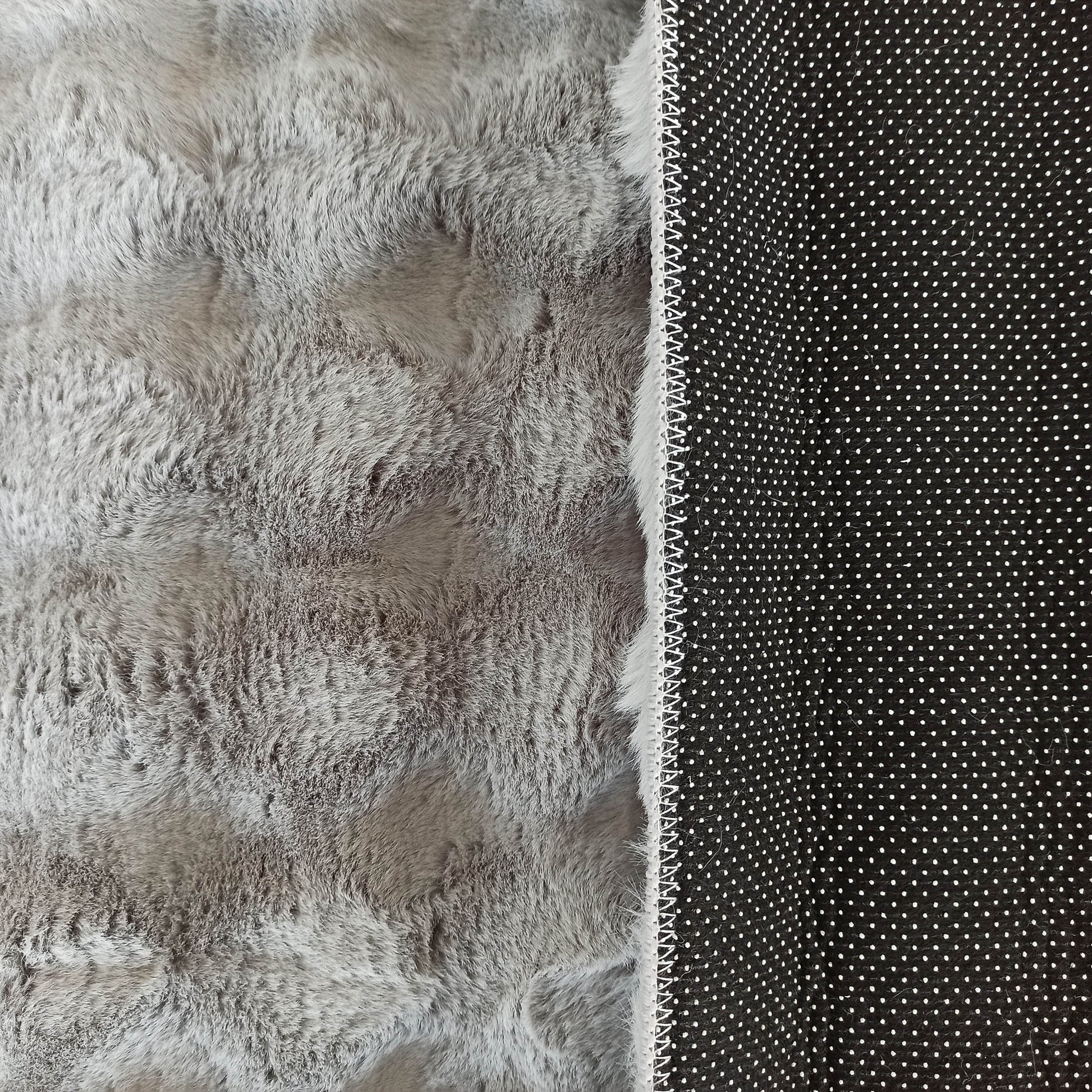 Tapis gris clair à poils longs, avec son envers noir parsemé de petits points blancs antidérapants et une couture blanche