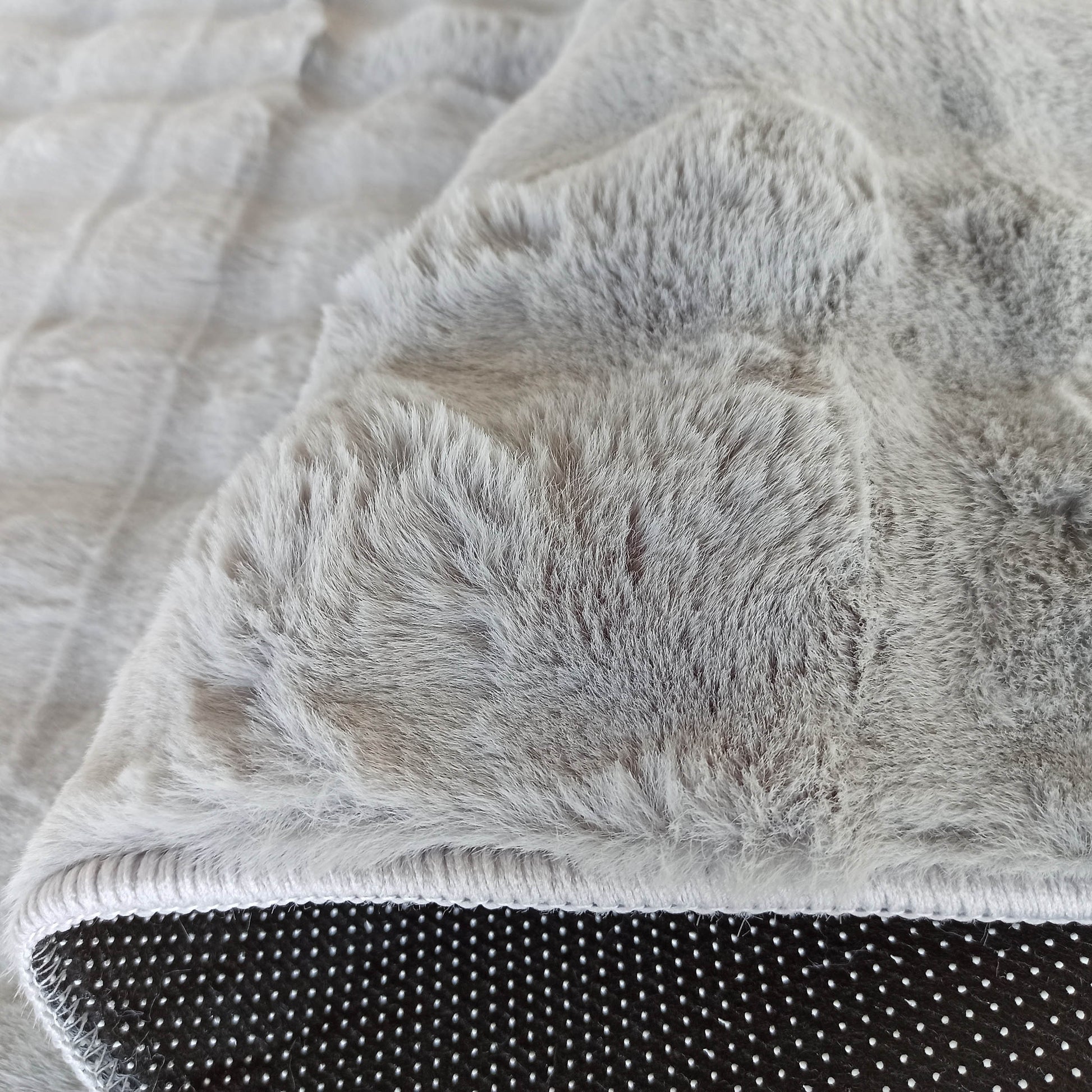 Tapis gris clair aux longues fibres douces, replié pour révéler son envers noir à motifs de picots antidérapants blancs