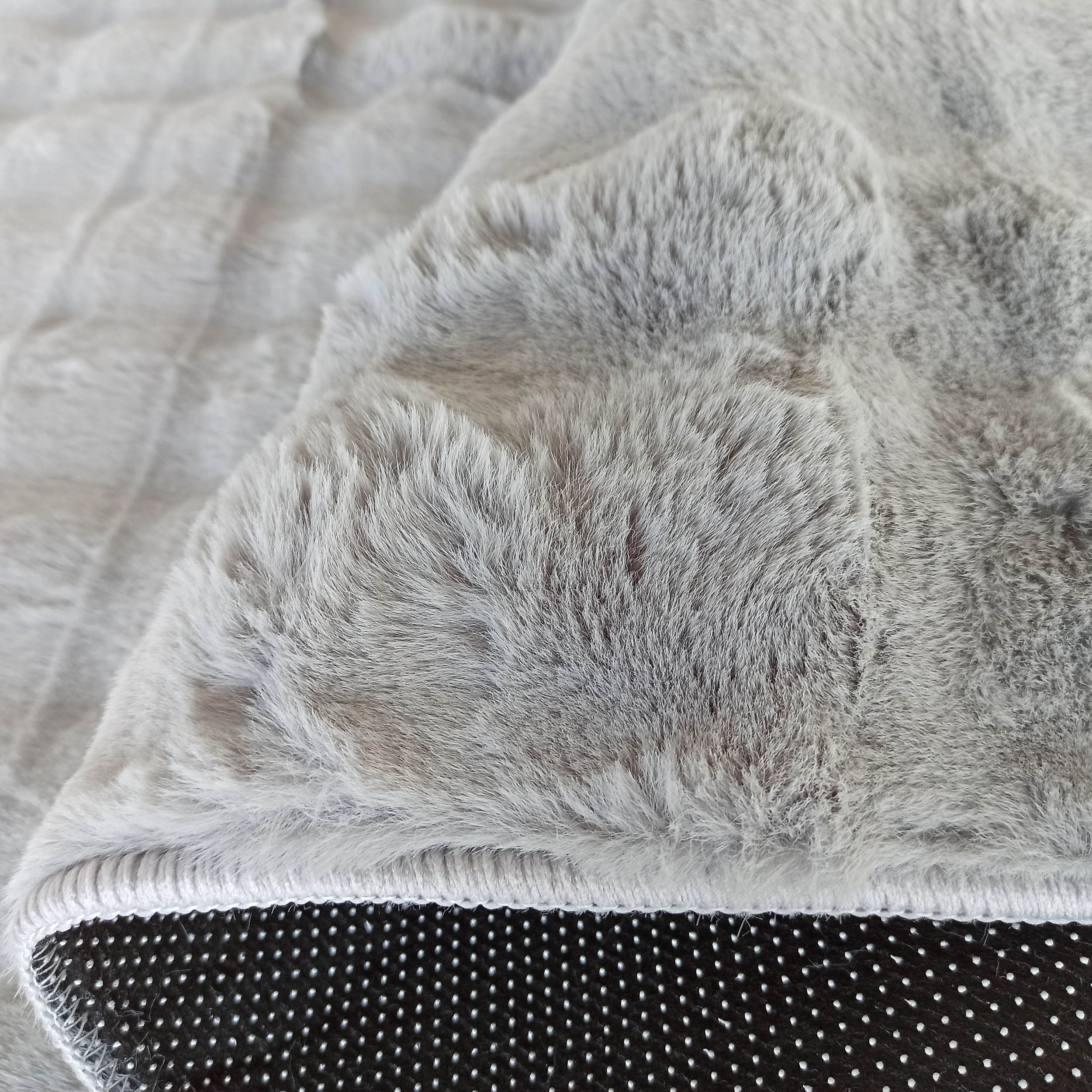 Tapis gris clair aux longues fibres douces, replié pour révéler son envers noir à motifs de picots antidérapants blancs