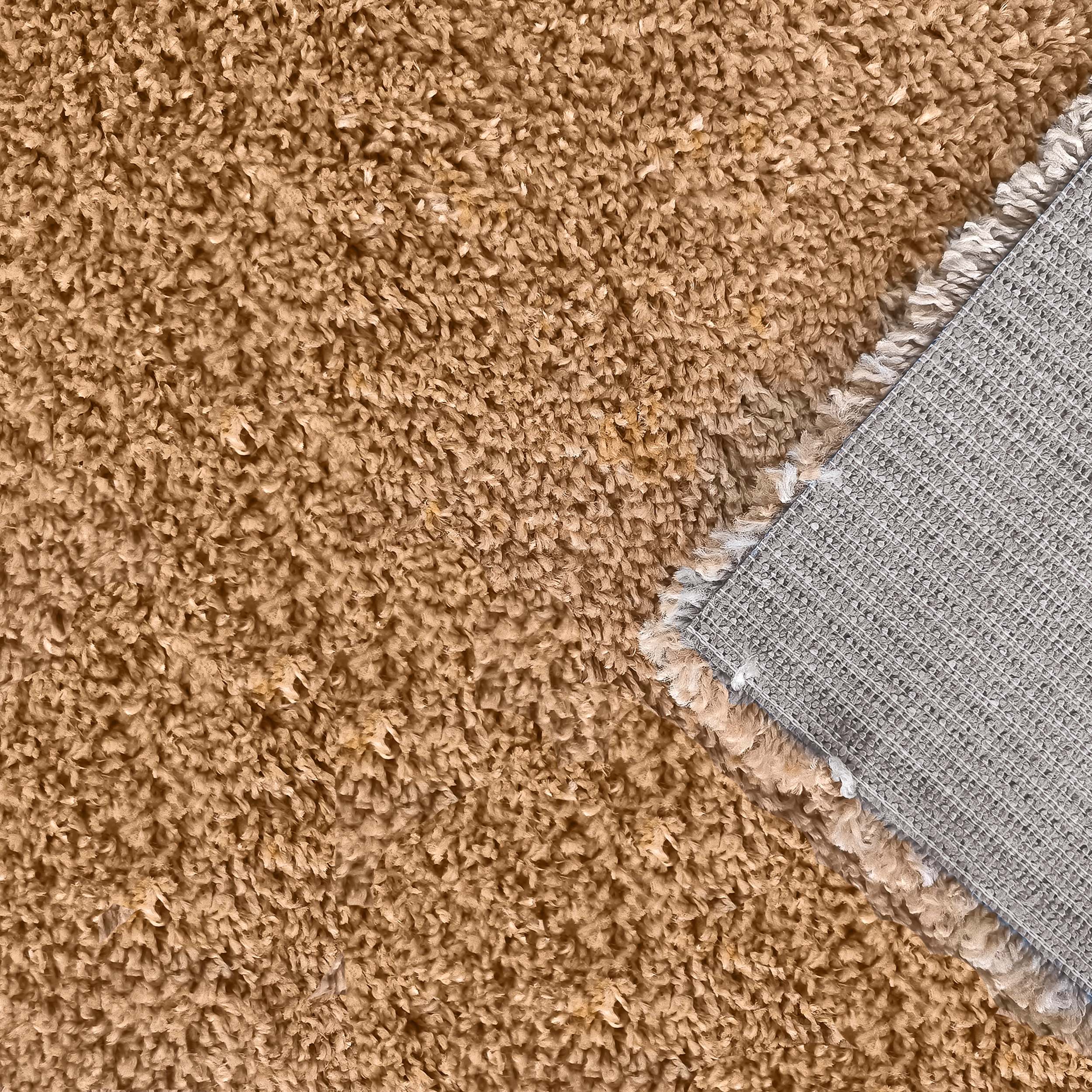 Tapis à poil long couleur camel dont un coin est retourné révélant la sous-face grise en grille