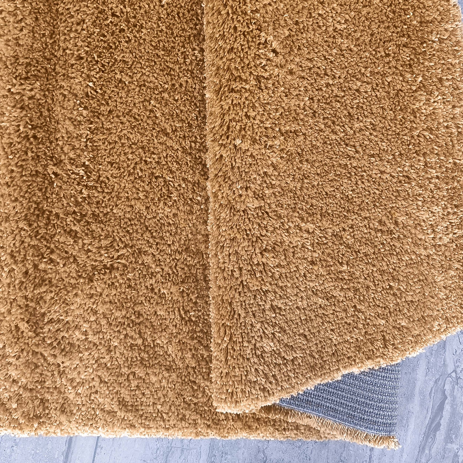 Tapis camel doux à poils longs et denses, partiellement replié, révélant son envers gris tissé sur un carrelage clair