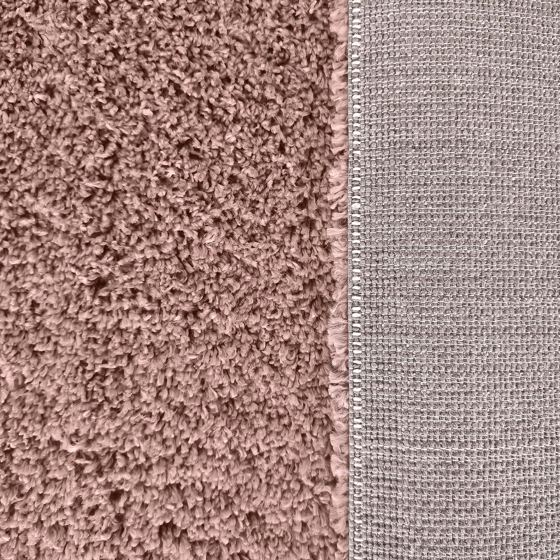Tapis rose poudré à poils longs contrastant avec son envers gris beige tissé en motif quadrillé