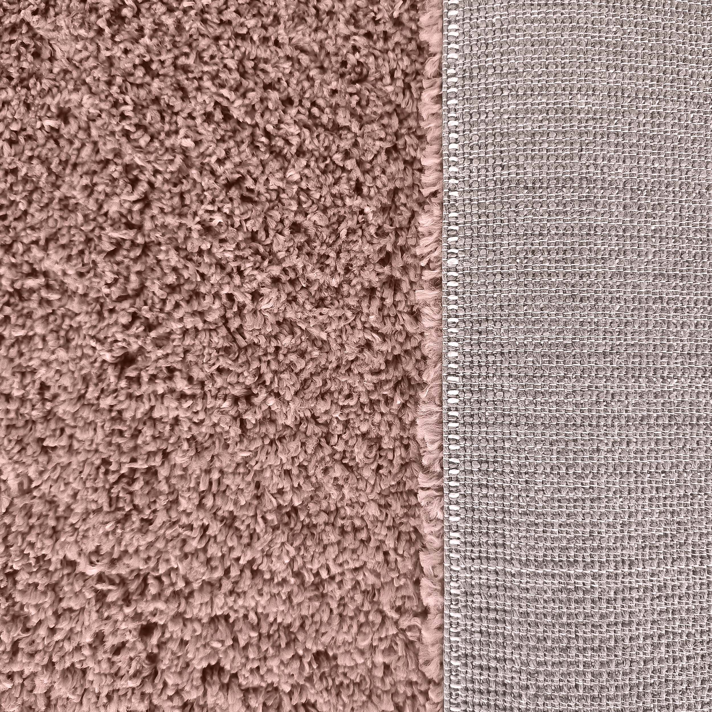 Tapis rose poudré à poils longs contrastant avec son envers gris beige tissé en motif quadrillé